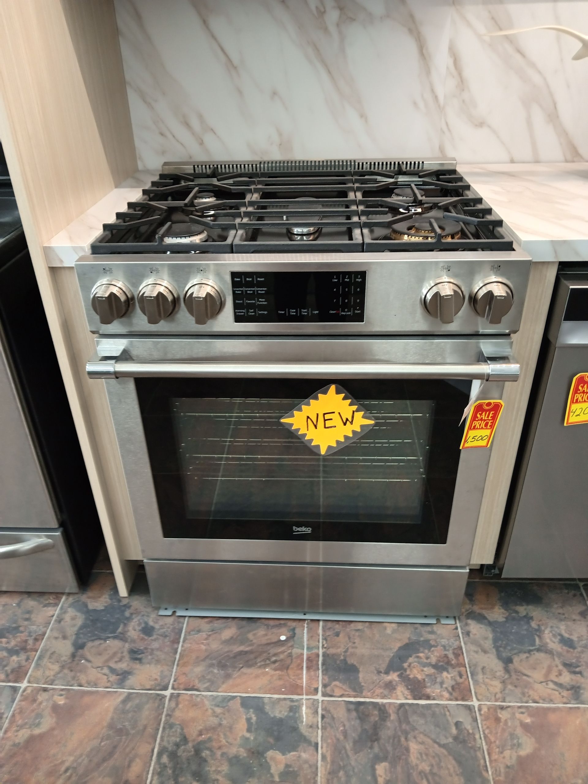 Stainless steel gas range with six burners and oven, in a kitchen showroom.
