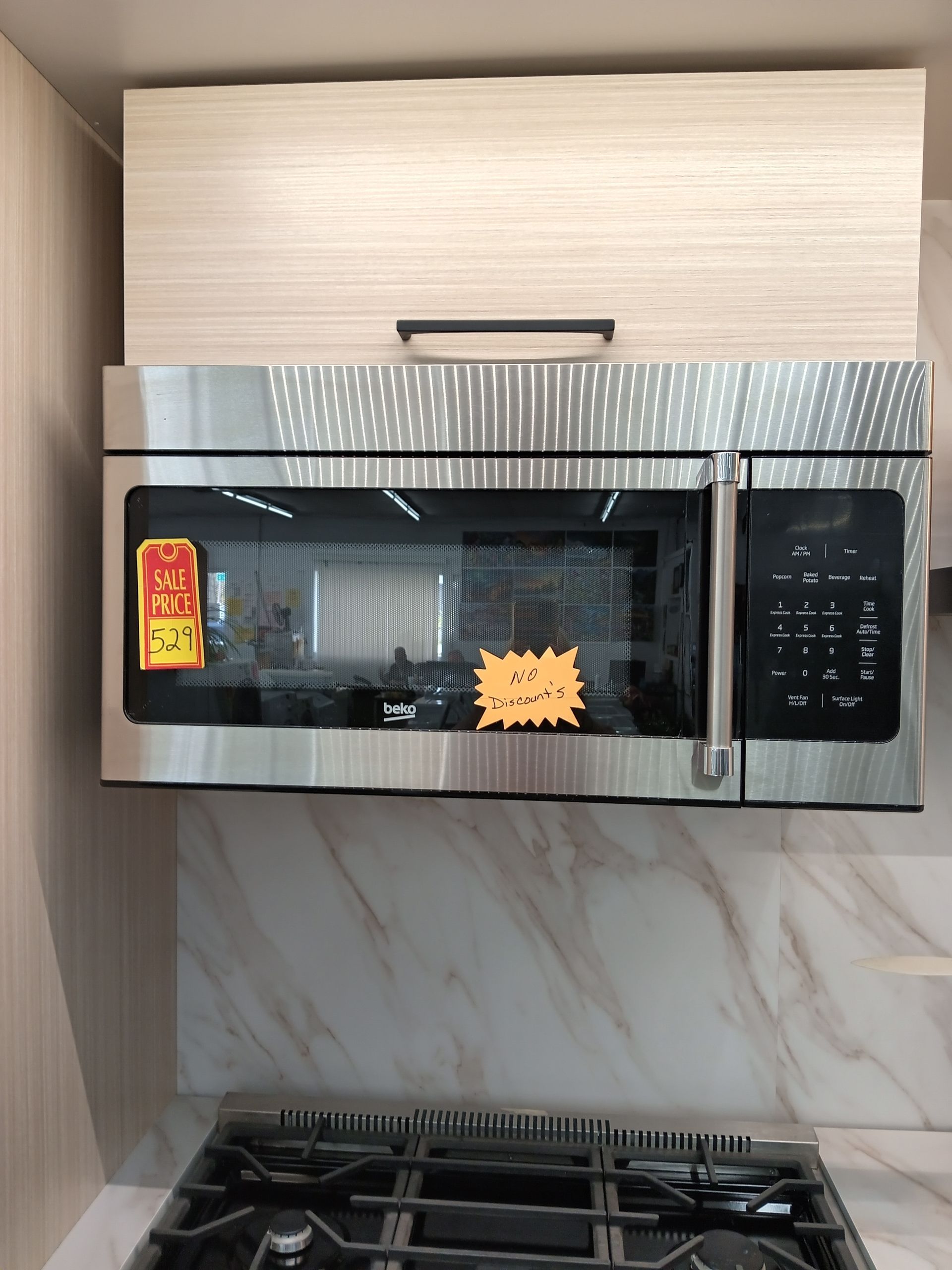 Over-the-range stainless steel microwave installed in kitchen. Cabinet above, gas stovetop below.