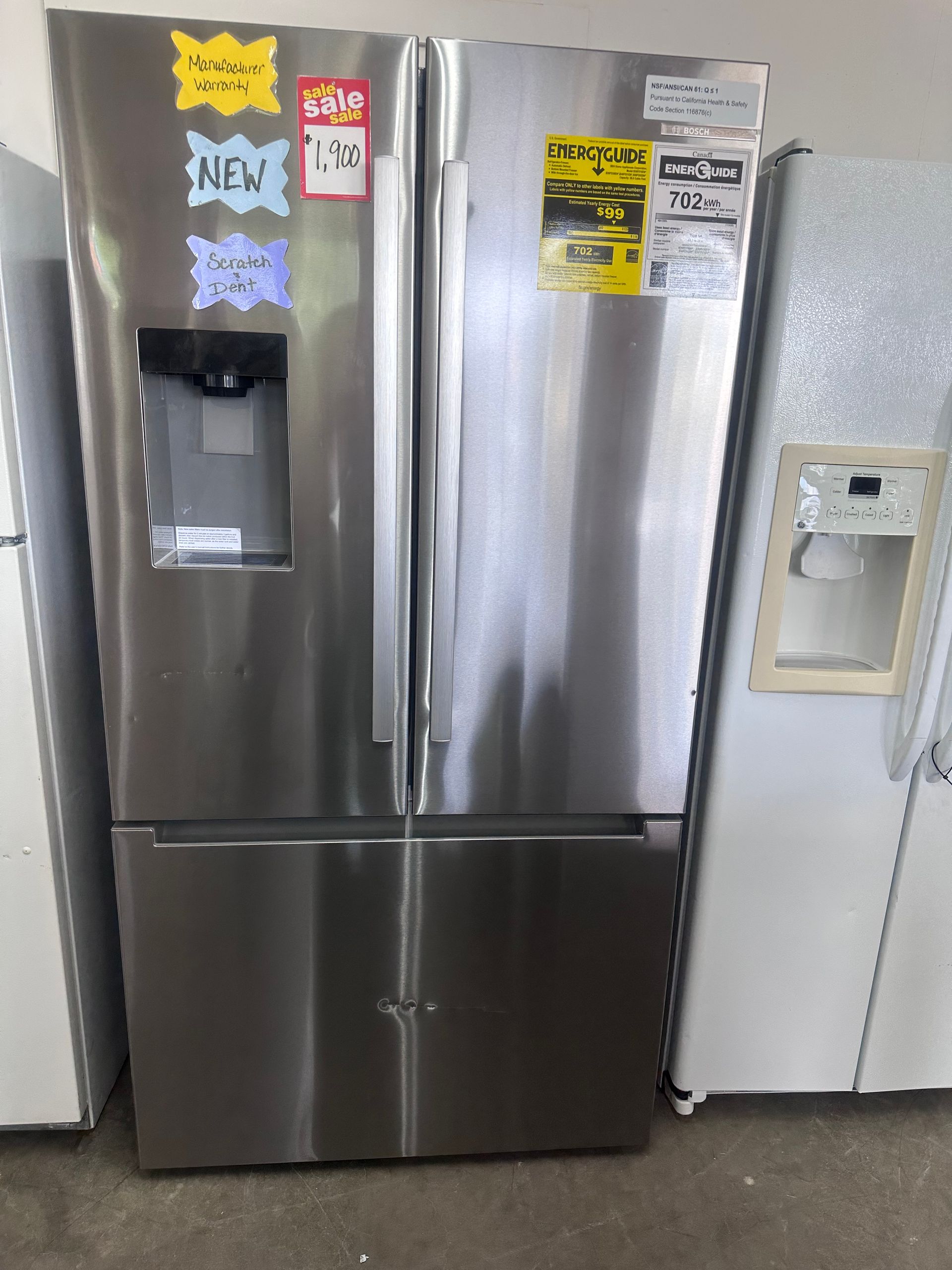Stainless steel French-door refrigerator with water dispenser in a showroom, with sale tags on the doors