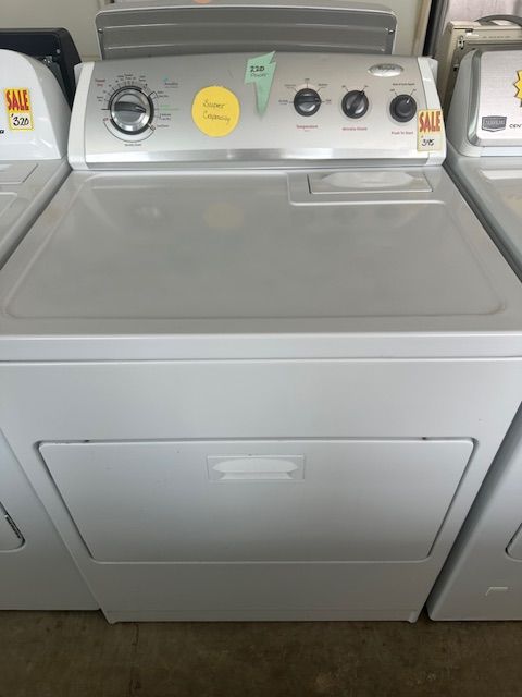 White top-load washing machine in a laundromat with coin controls and a front access panel.