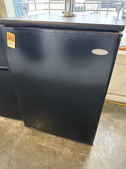 A black refrigerator is sitting on a concrete floor in a store.