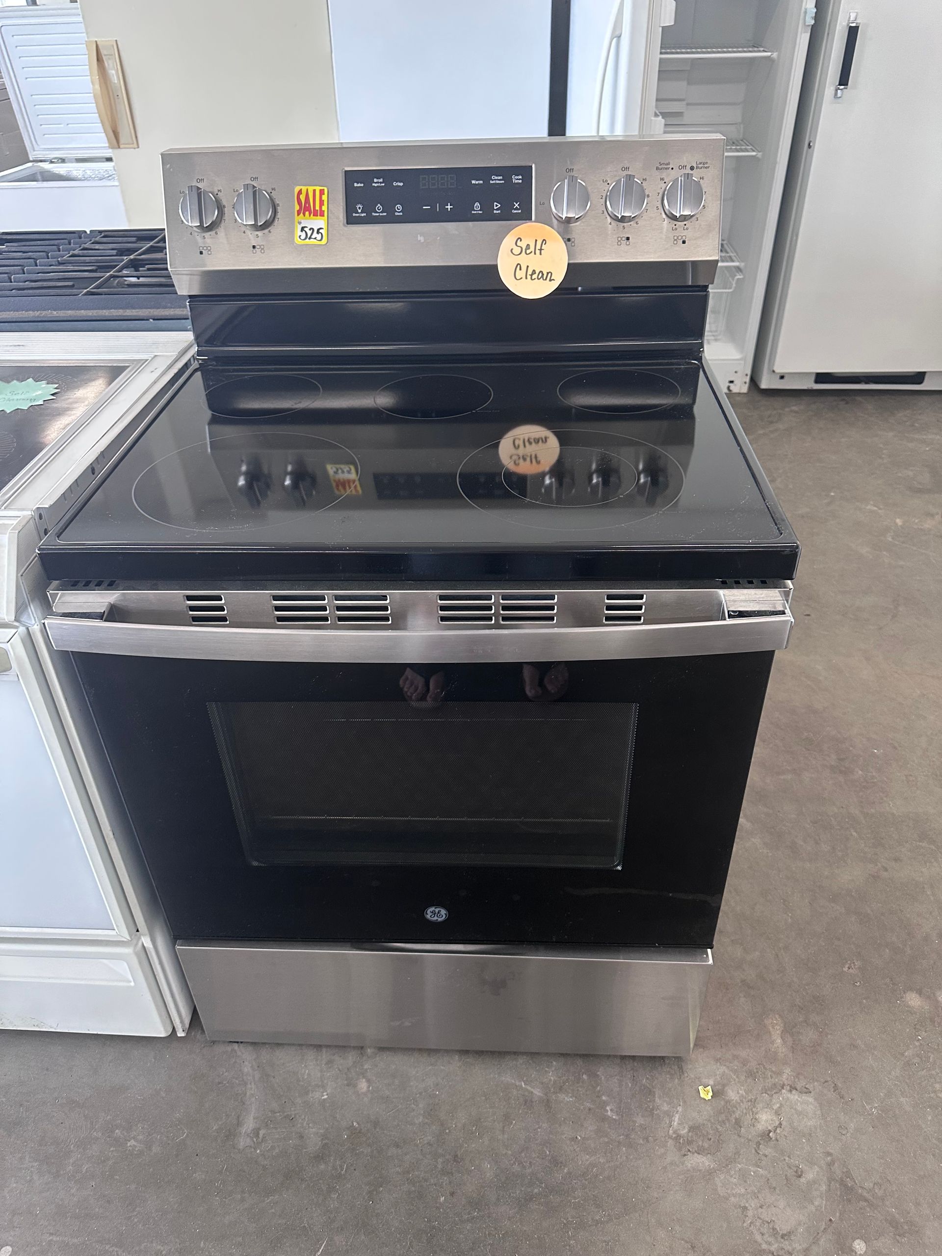 A stainless steel stove with a black glass top is sitting on a concrete floor.