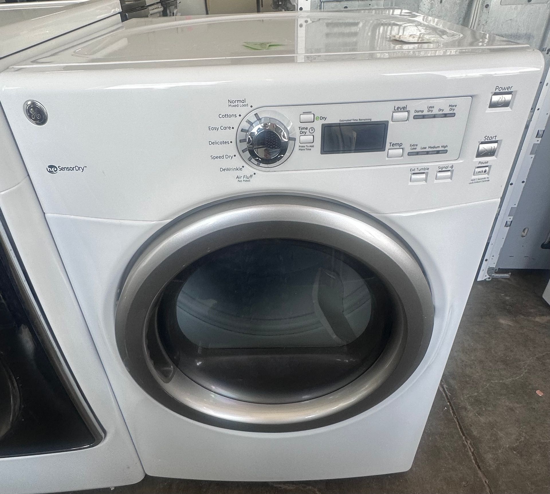 White front-loading washing machine with control dial and display in a store or laundry area