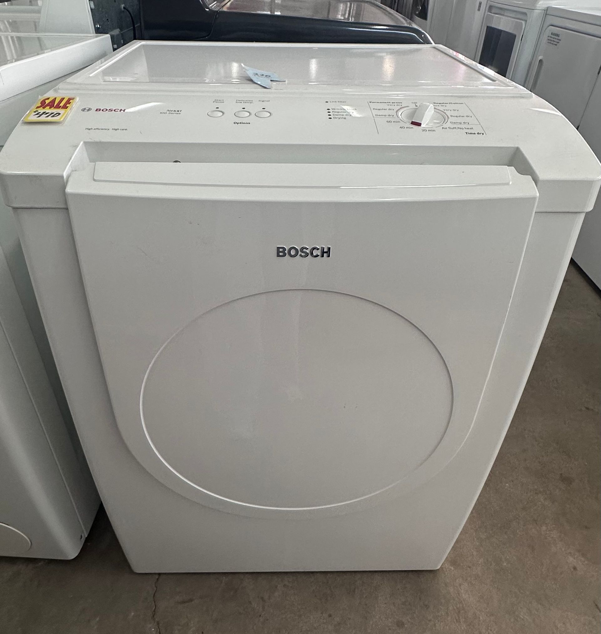 White Bosch front-load dryer in a showroom, with control panel on top and circular door front.