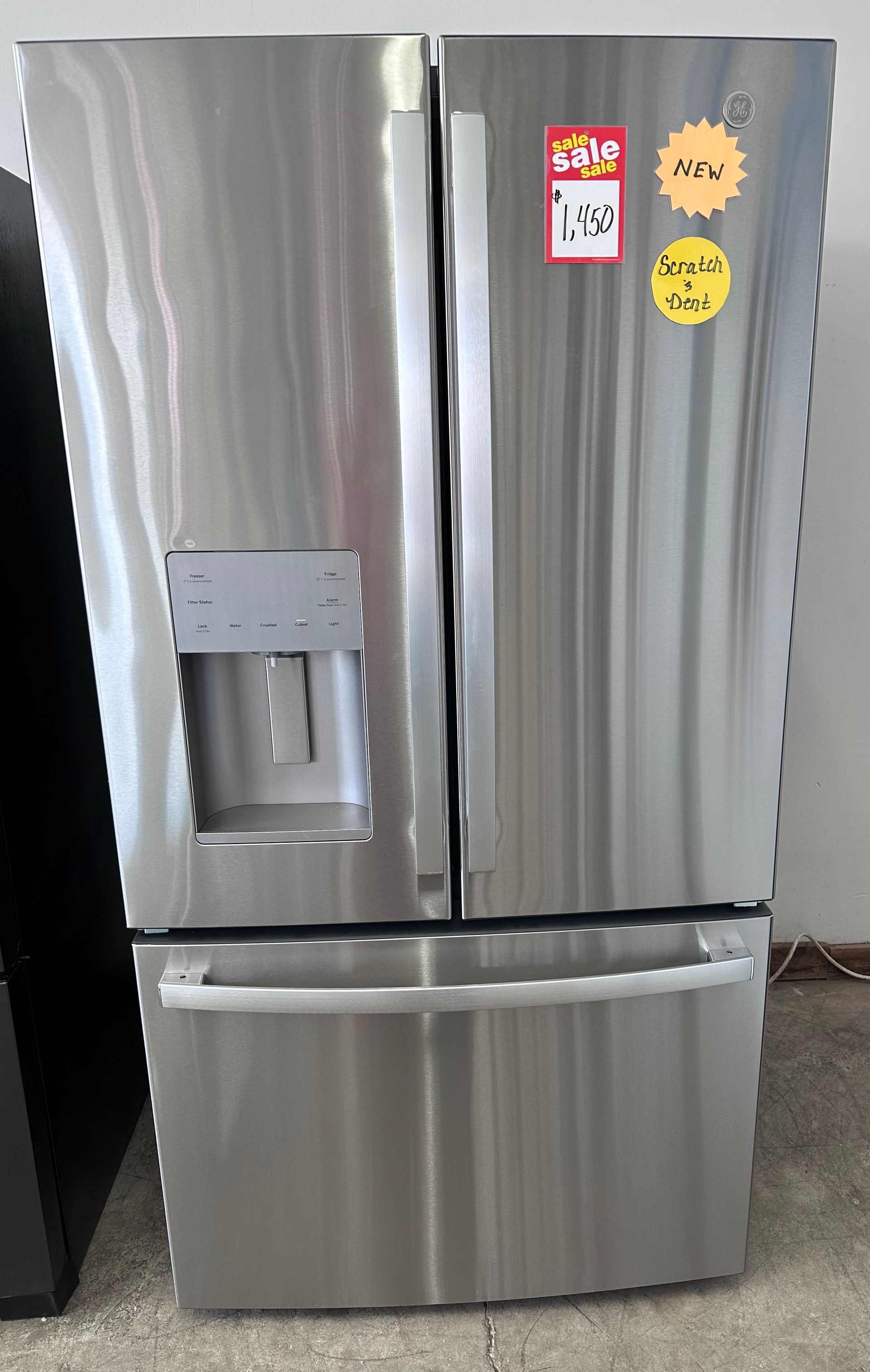White refrigerator, top-freezer style, with blue tape securing doors. A yellow energy efficiency sticker and sale tag are visible.