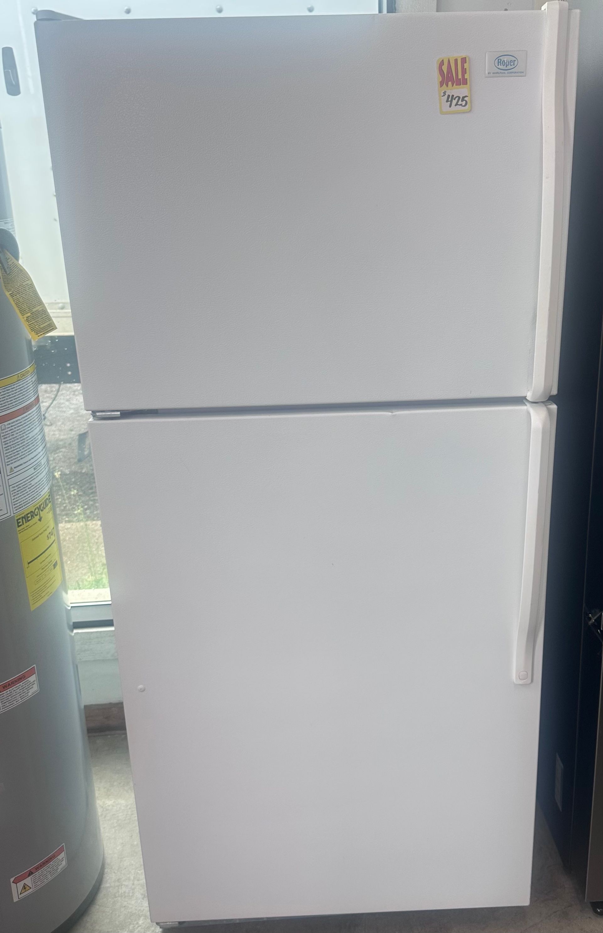 White top-freezer refrigerator standing in a kitchen or store area.