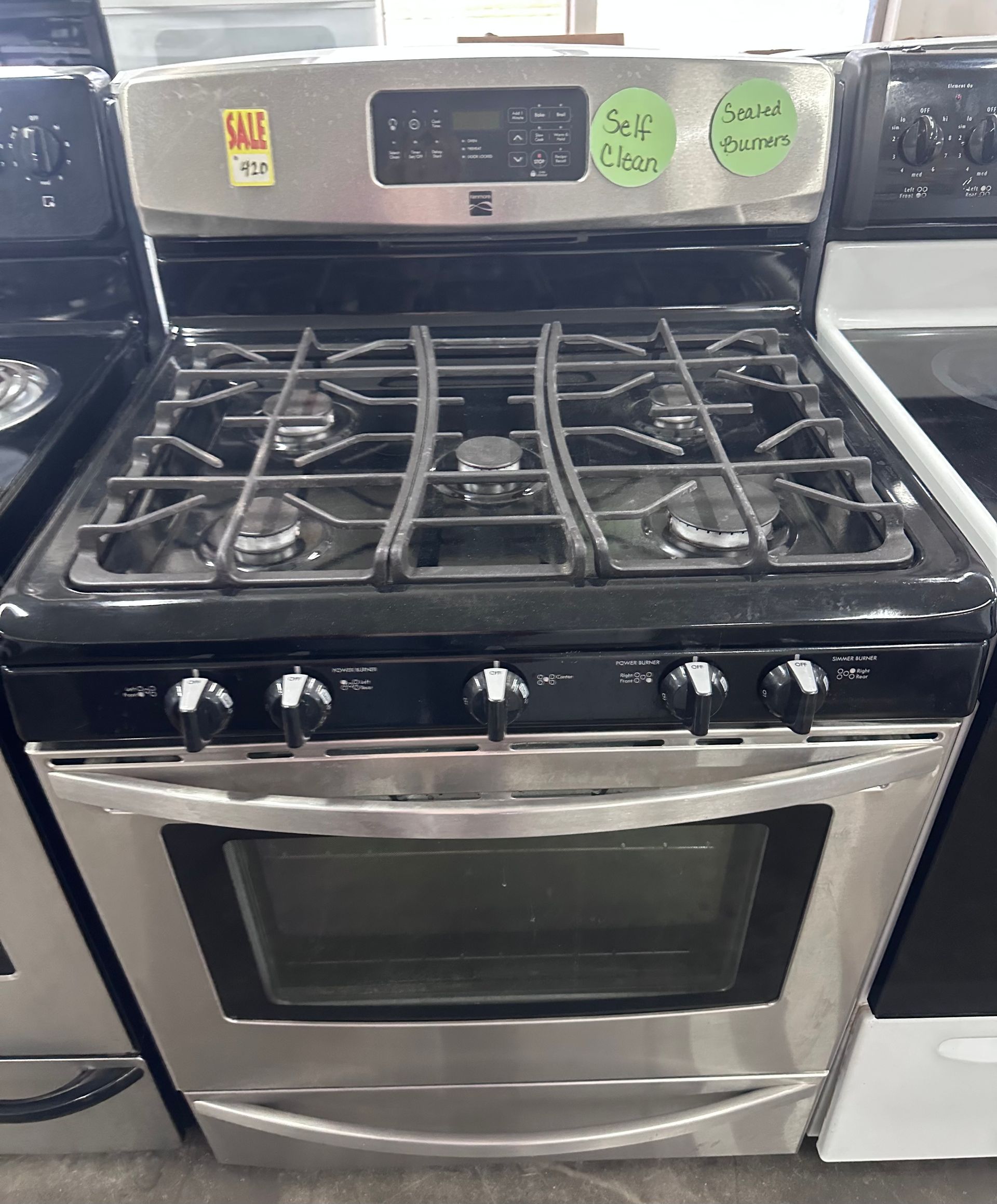 Stainless steel gas range with black cooktop and oven door in a kitchen display