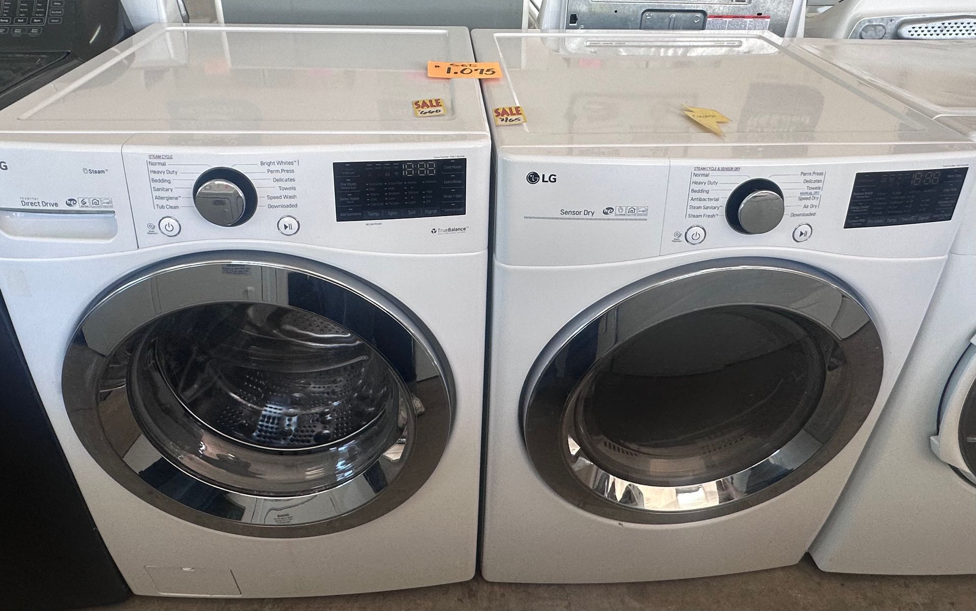 A white washing machine with the lid open is sitting next to another washing machine.