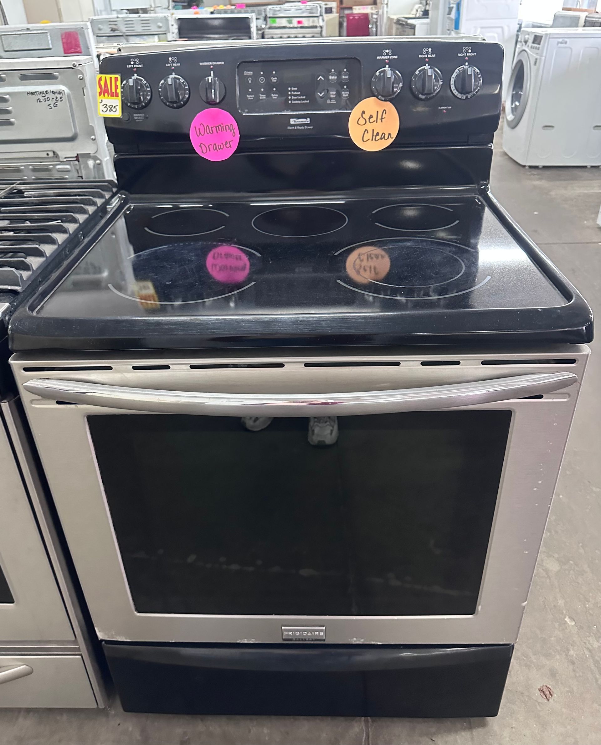 Black stainless steel electric oven with stovetop in a store display, with sale stickers on the control panel.