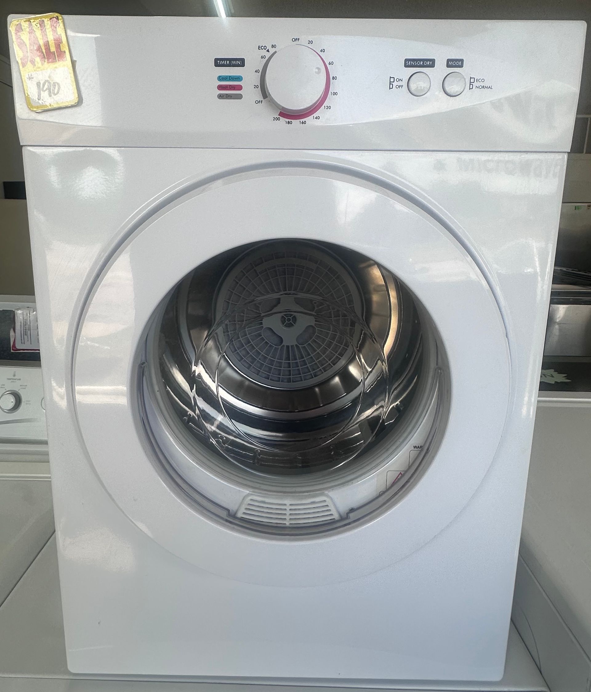 White front-loading washing machine in a laundry room, with a round glass door and control panel on top.