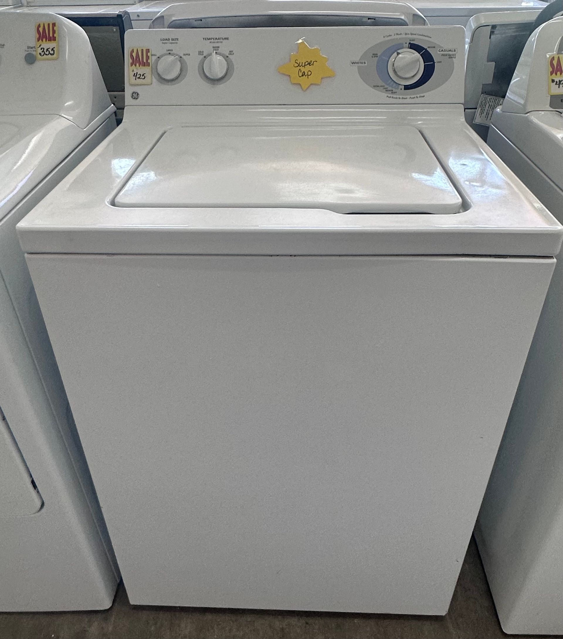 LG washing machine on sale for $1,200, with a person reflected in the dark glass door.