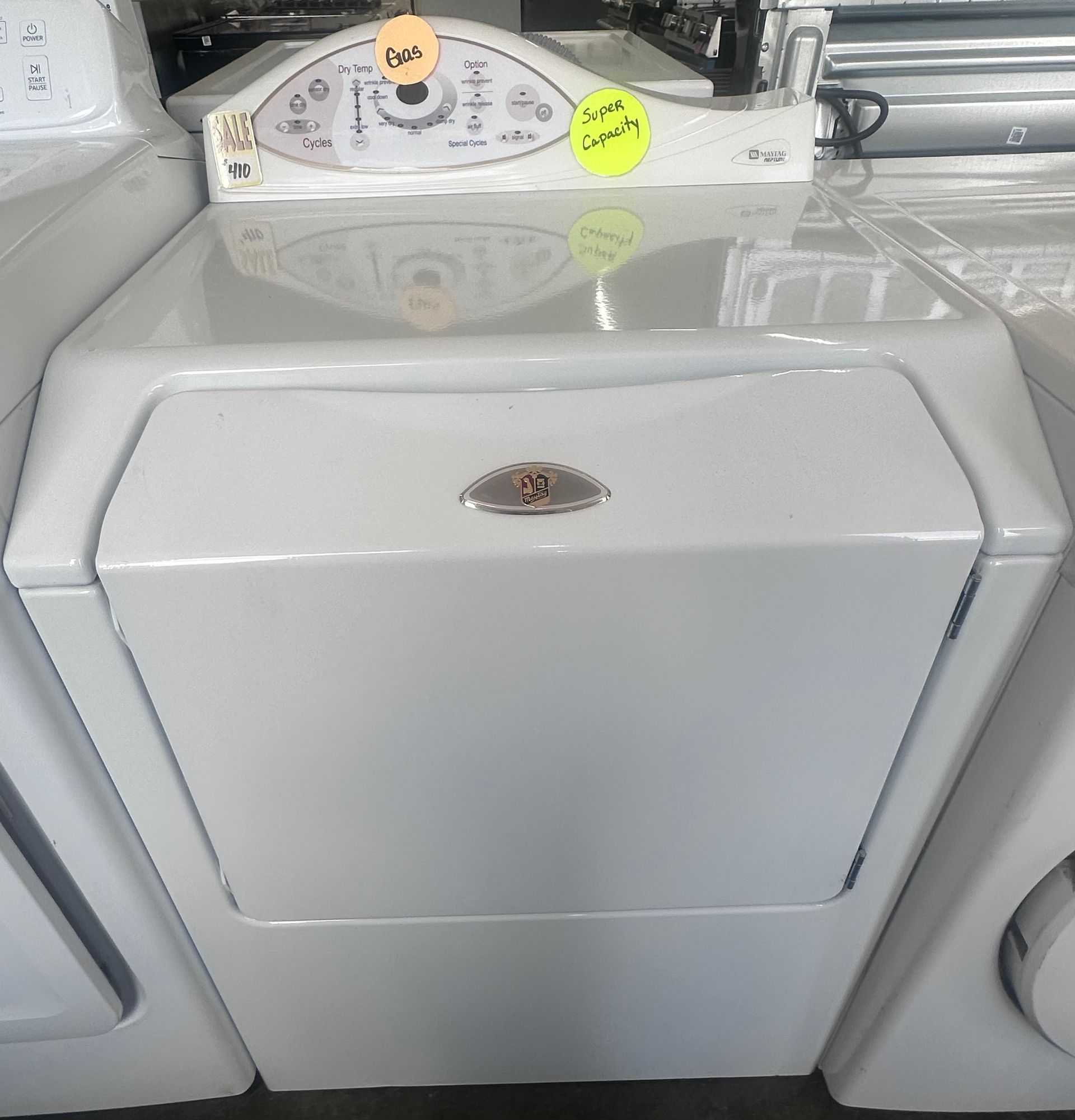 White dryer in a laundromat, with a folded control panel and coin slots visible on top.