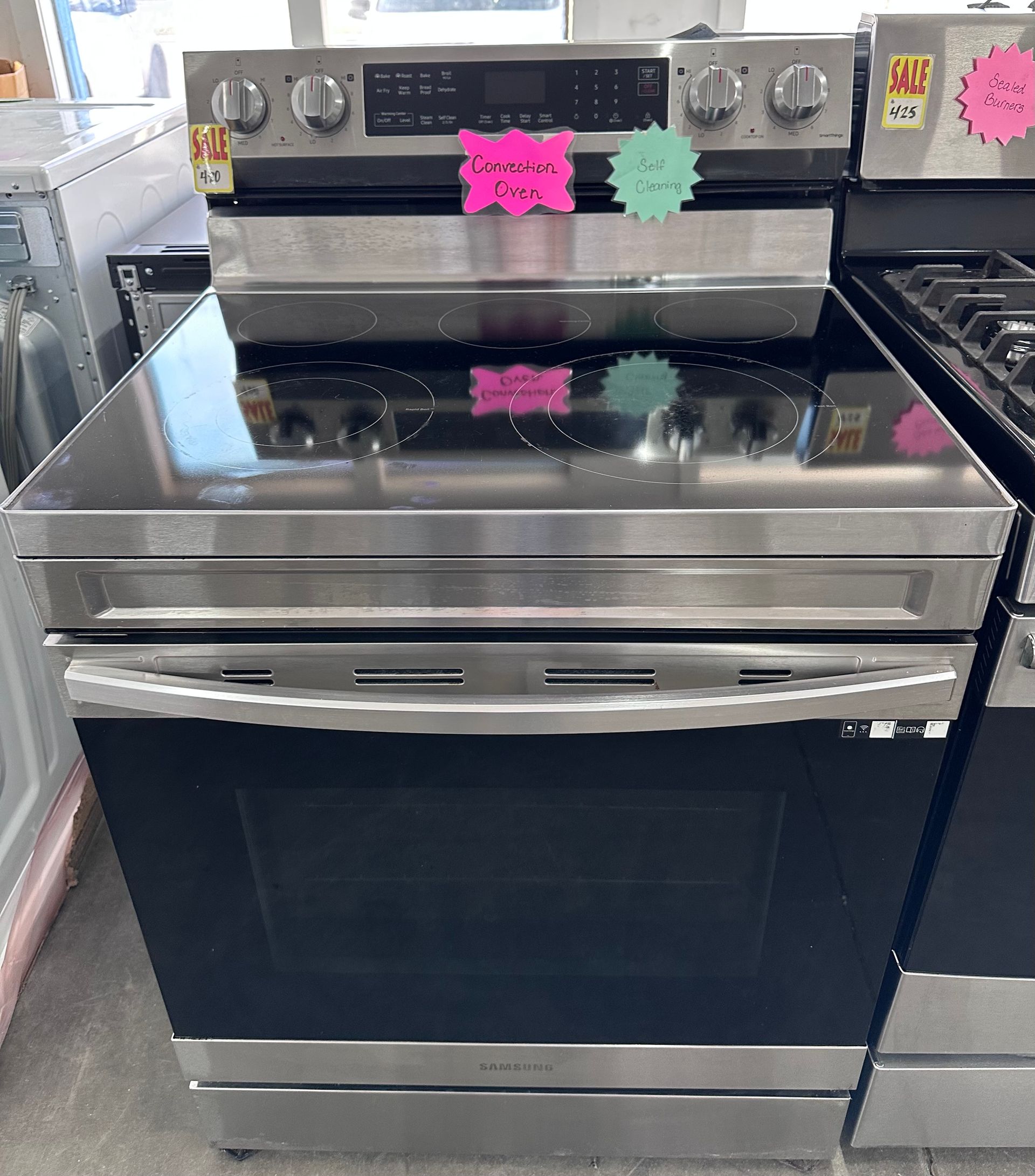 Stainless steel electric stove with black oven door in a kitchen, decorated with pink and green magnets.