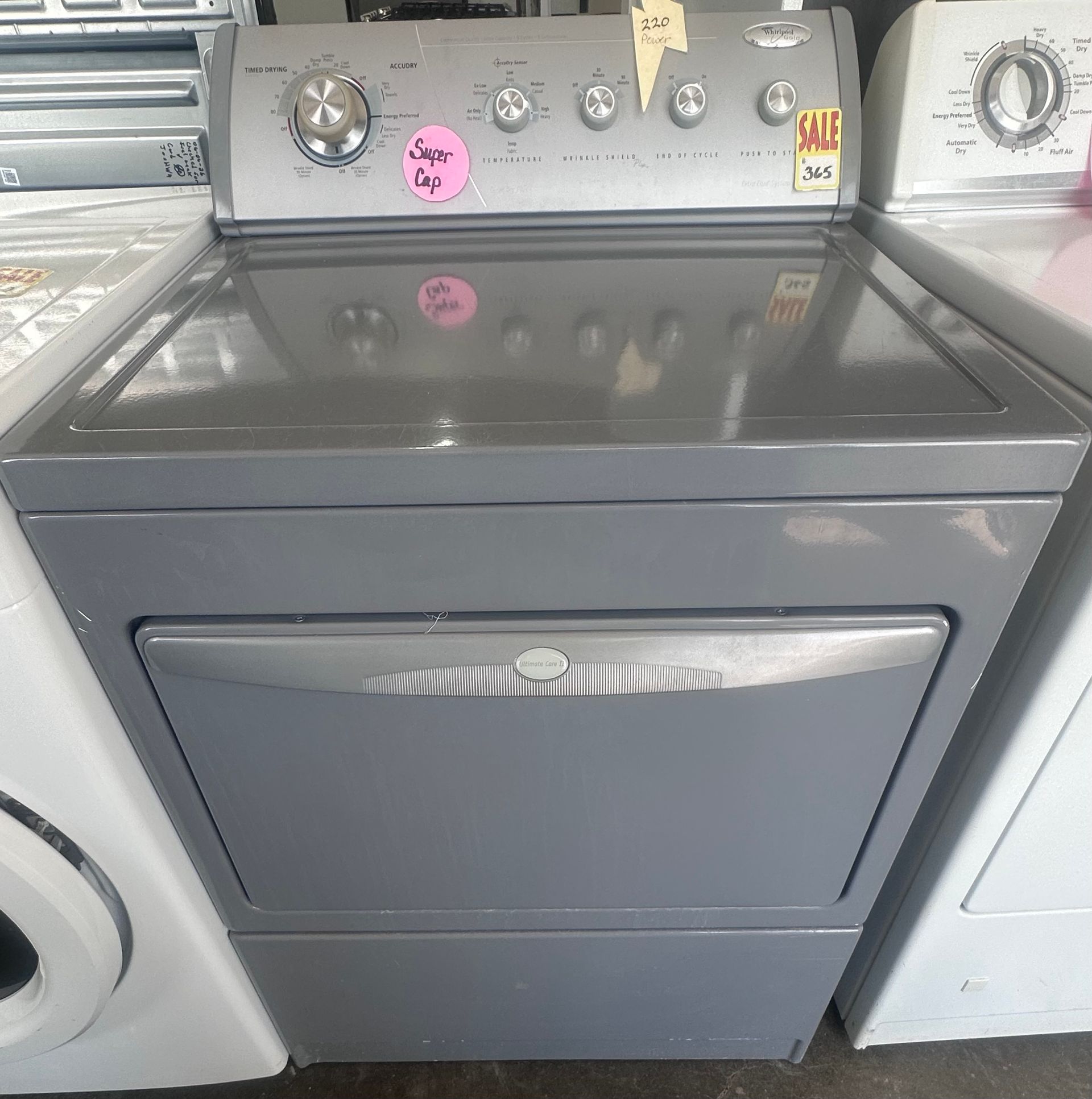 Gray top-load dryer in a laundromat, shown between two other machines.