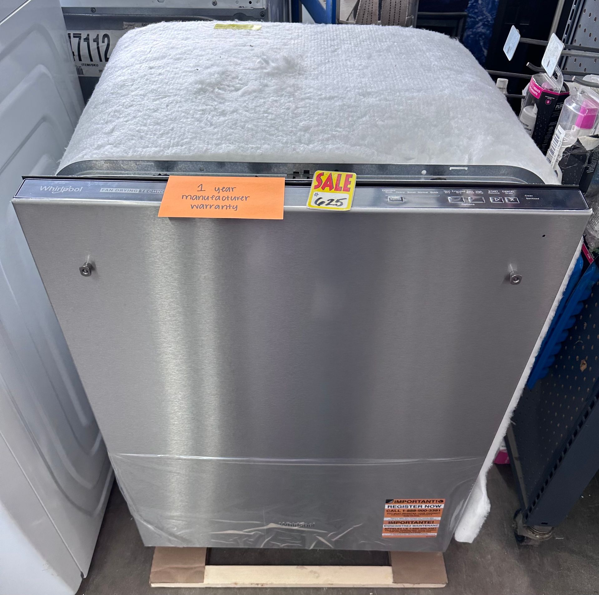 Stainless steel dishwasher with a sale tag, sitting on a wooden pallet in a store.