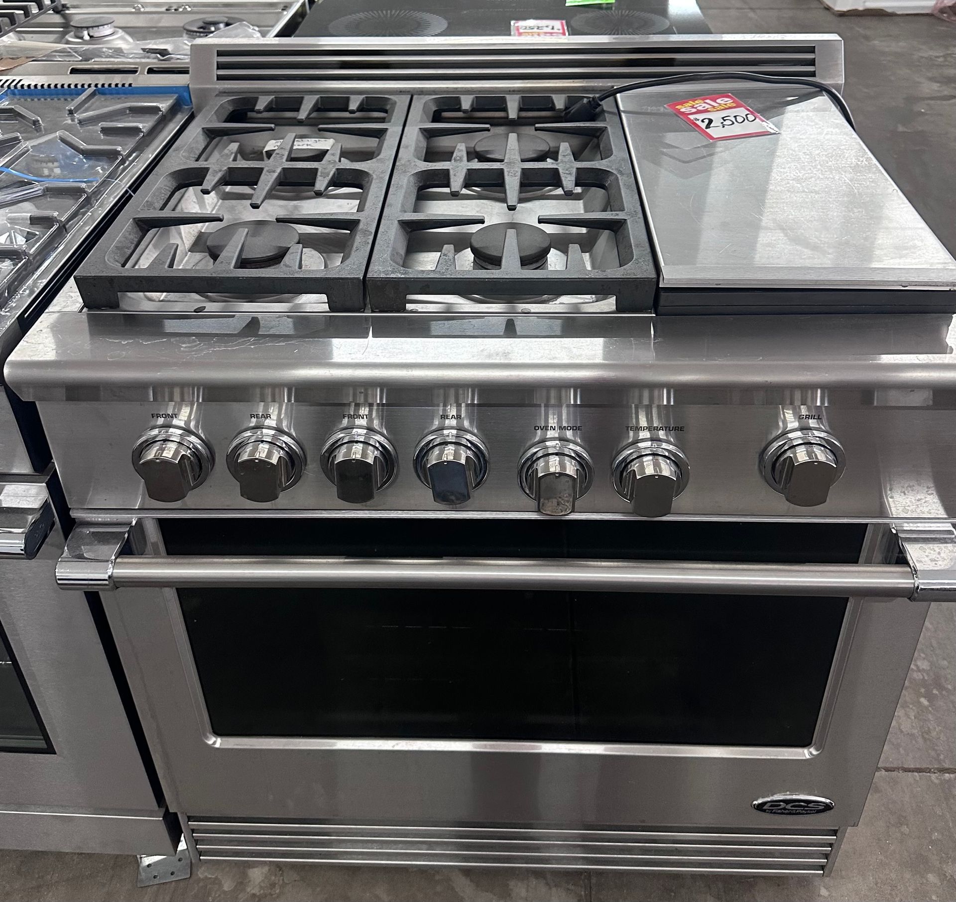 Stainless steel gas range oven with six knobs and grates in a store display