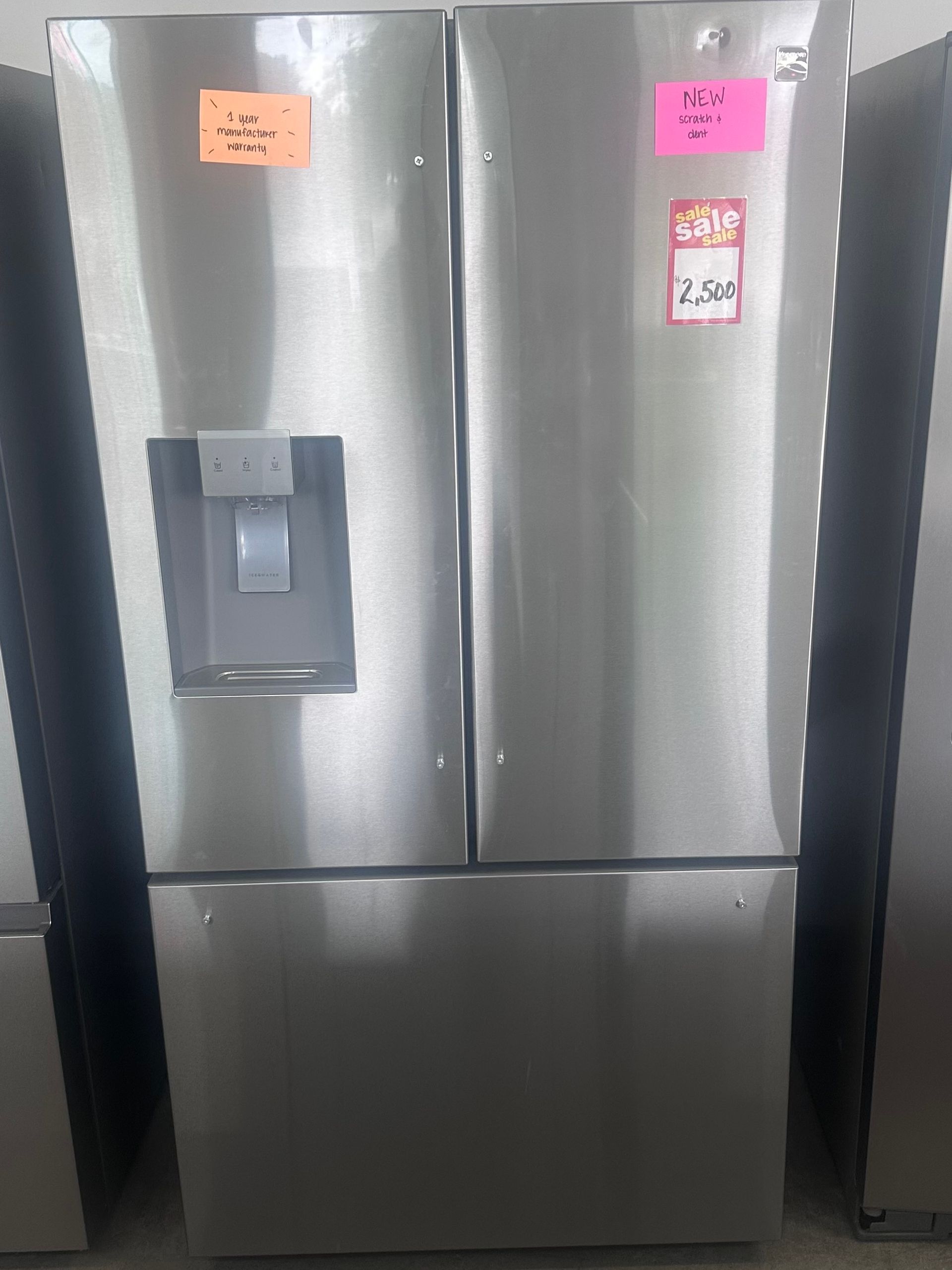 A stainless steel side-by-side refrigerator with a water dispenser, taped doors, and price labels attached.