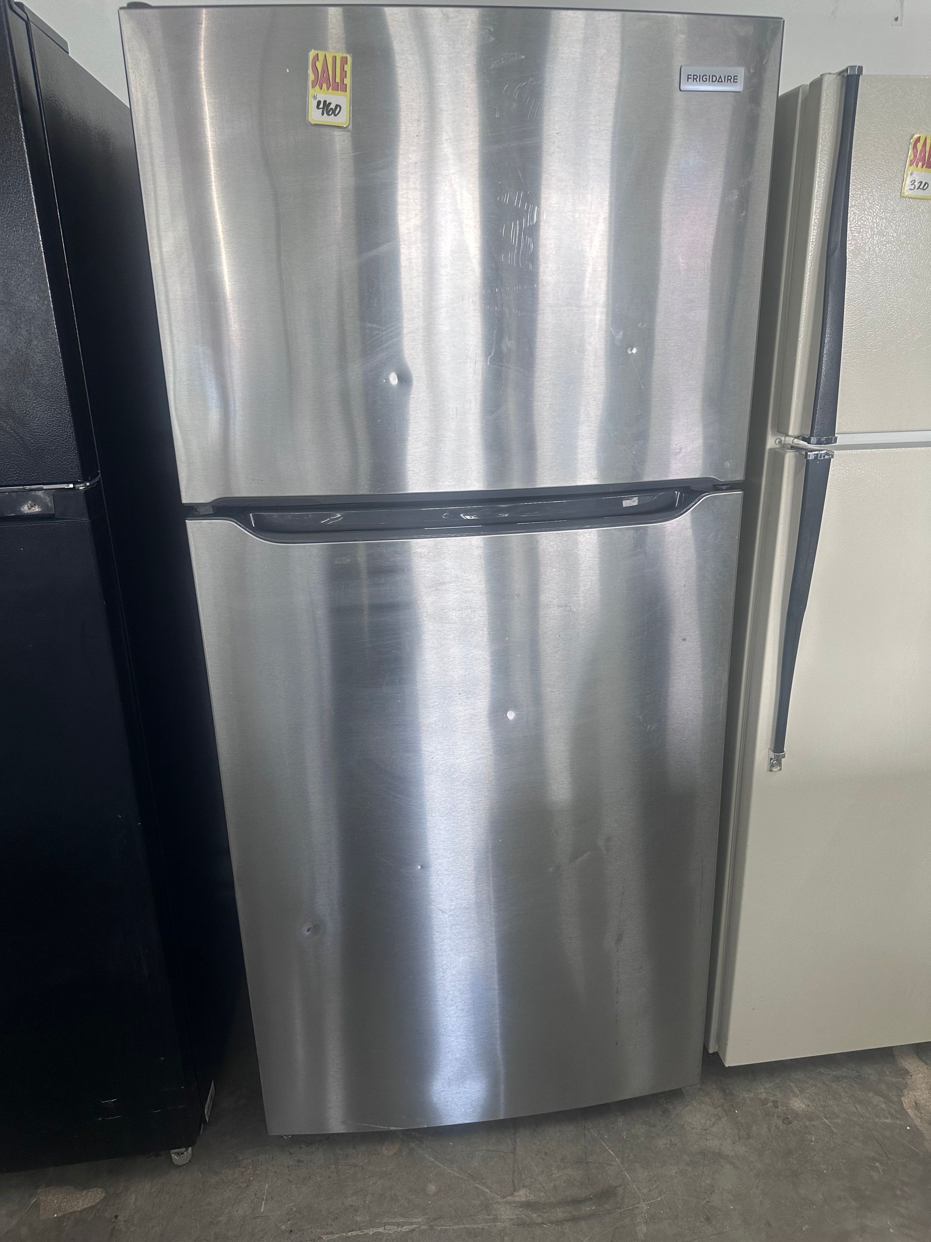 Stainless steel refrigerator between two other appliances on a kitchen floor.