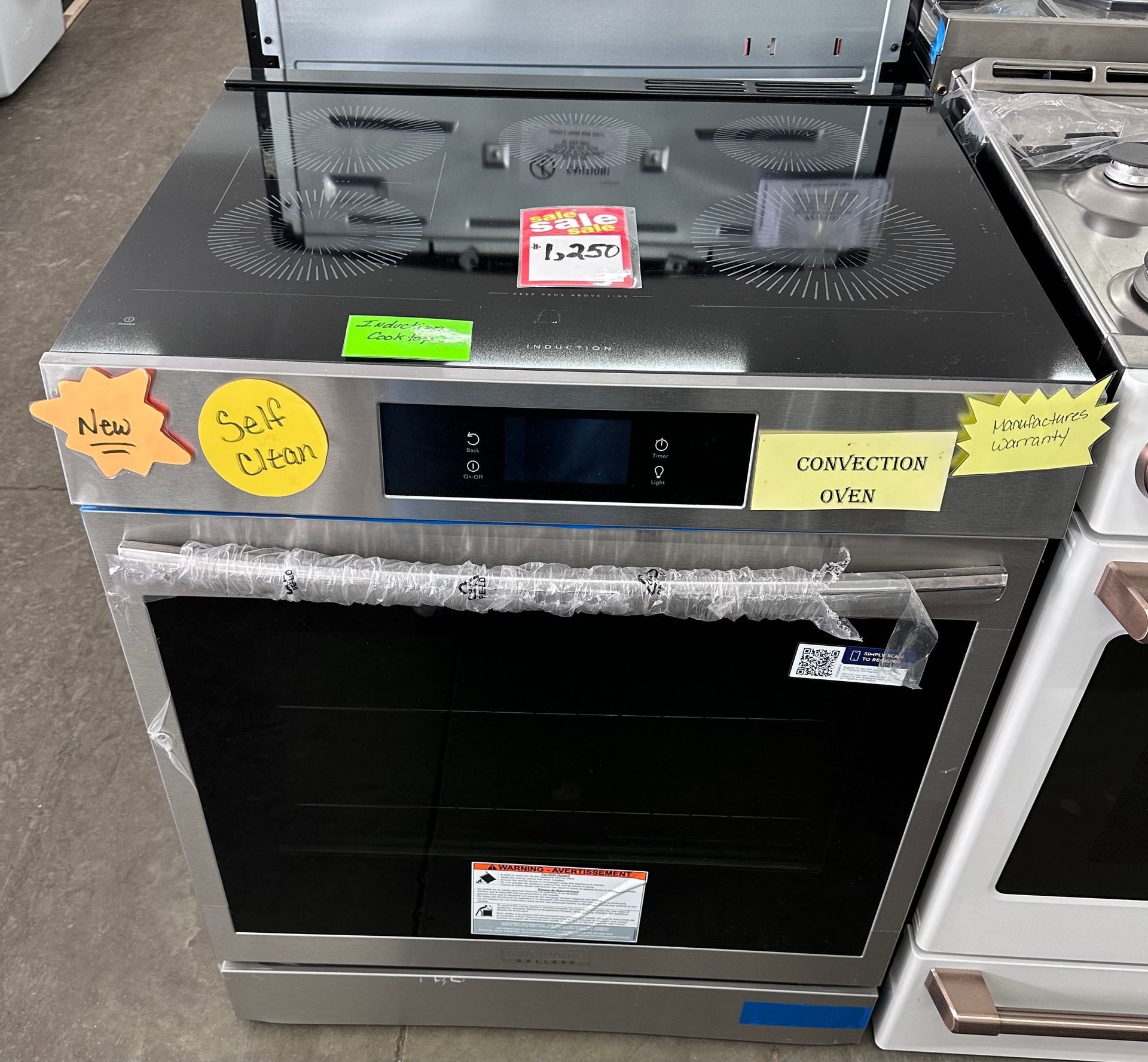 Stainless steel built-in oven with induction cooktop on display. Price tags and labels are visible.