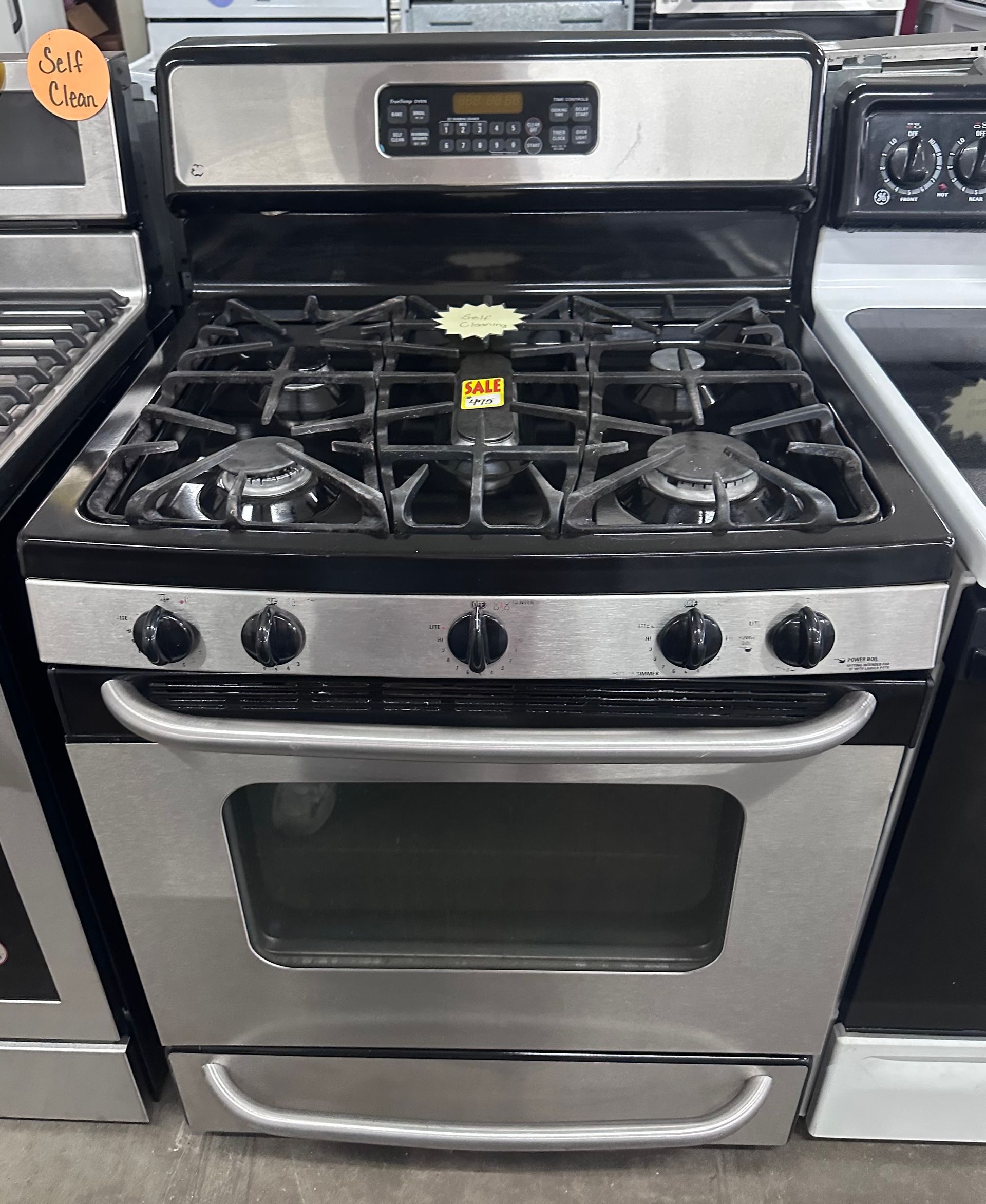 Stainless steel gas range oven with four burners and black control knobs in an appliance showroom