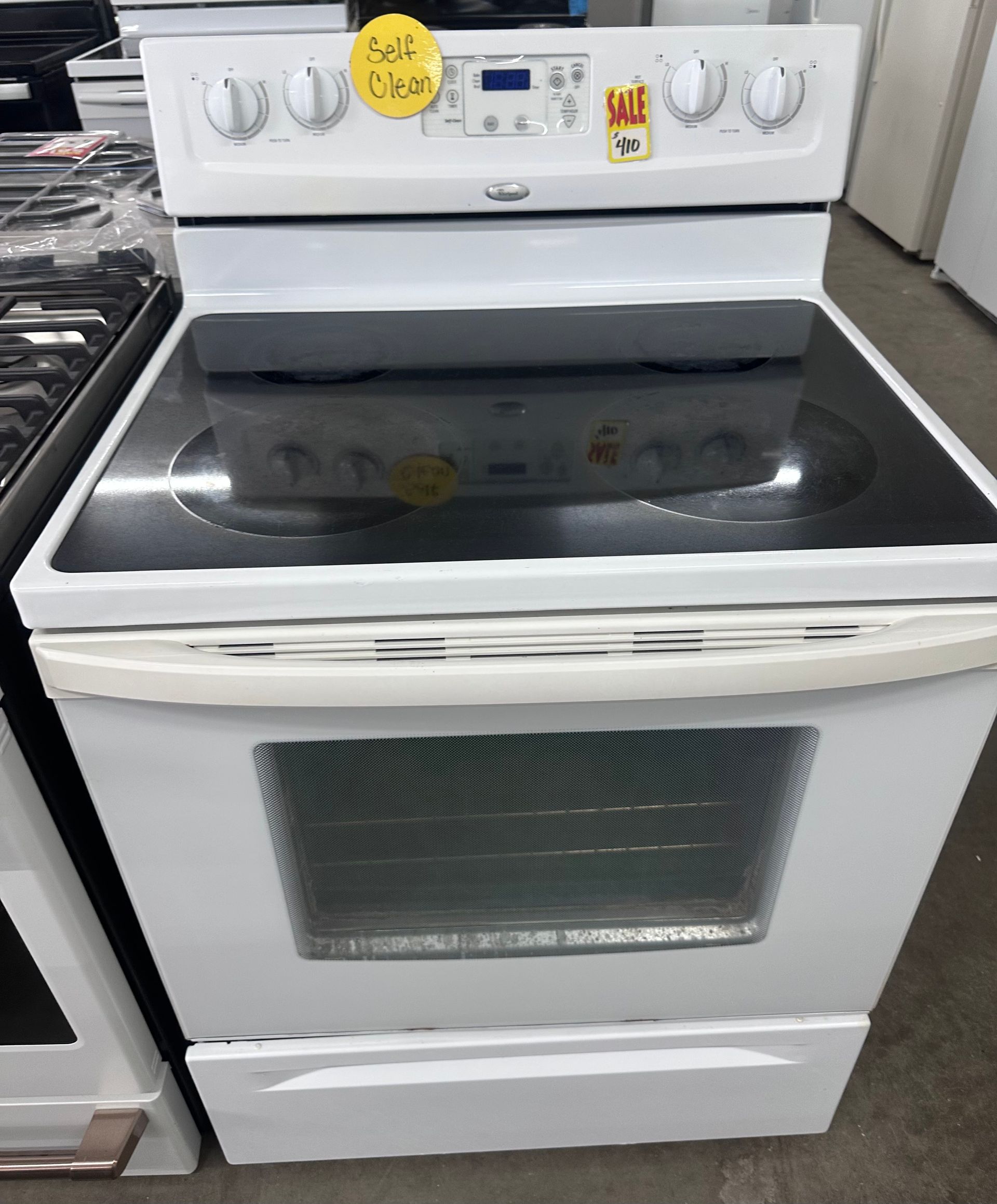 White electric stove with black glass cooktop and oven door in a kitchen showroom.