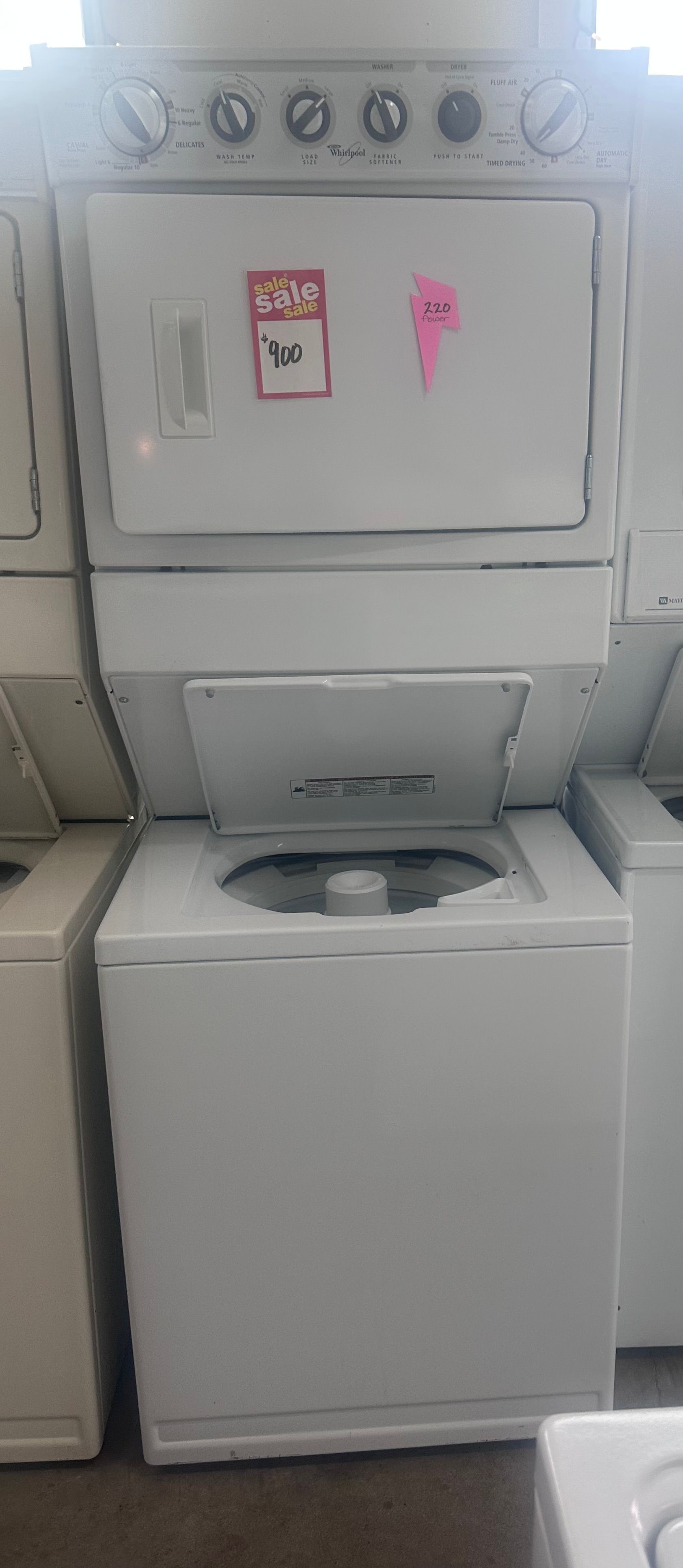 Laundry room with stacked washer and dryer, top machine door open and lower washer lid closed.