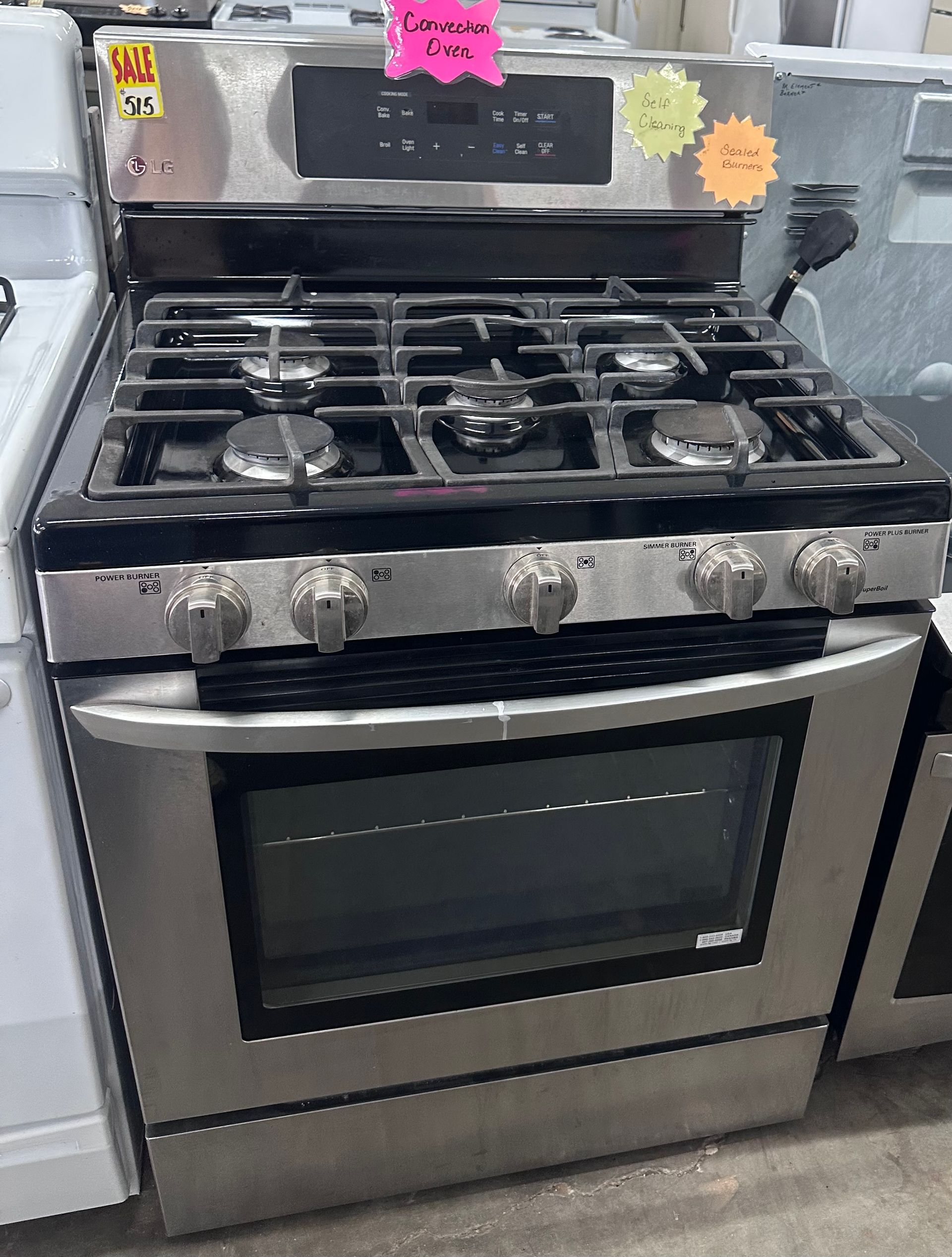 Stainless steel gas range oven with five burners, displayed in an appliance store.