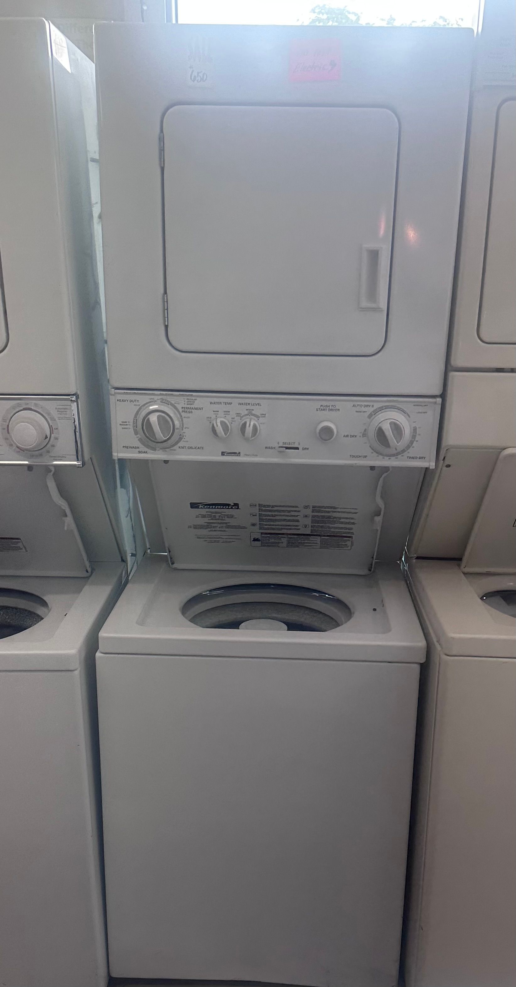 Stacked washer and dryer in a laundry room, with the washer lid open and dryer controls above.