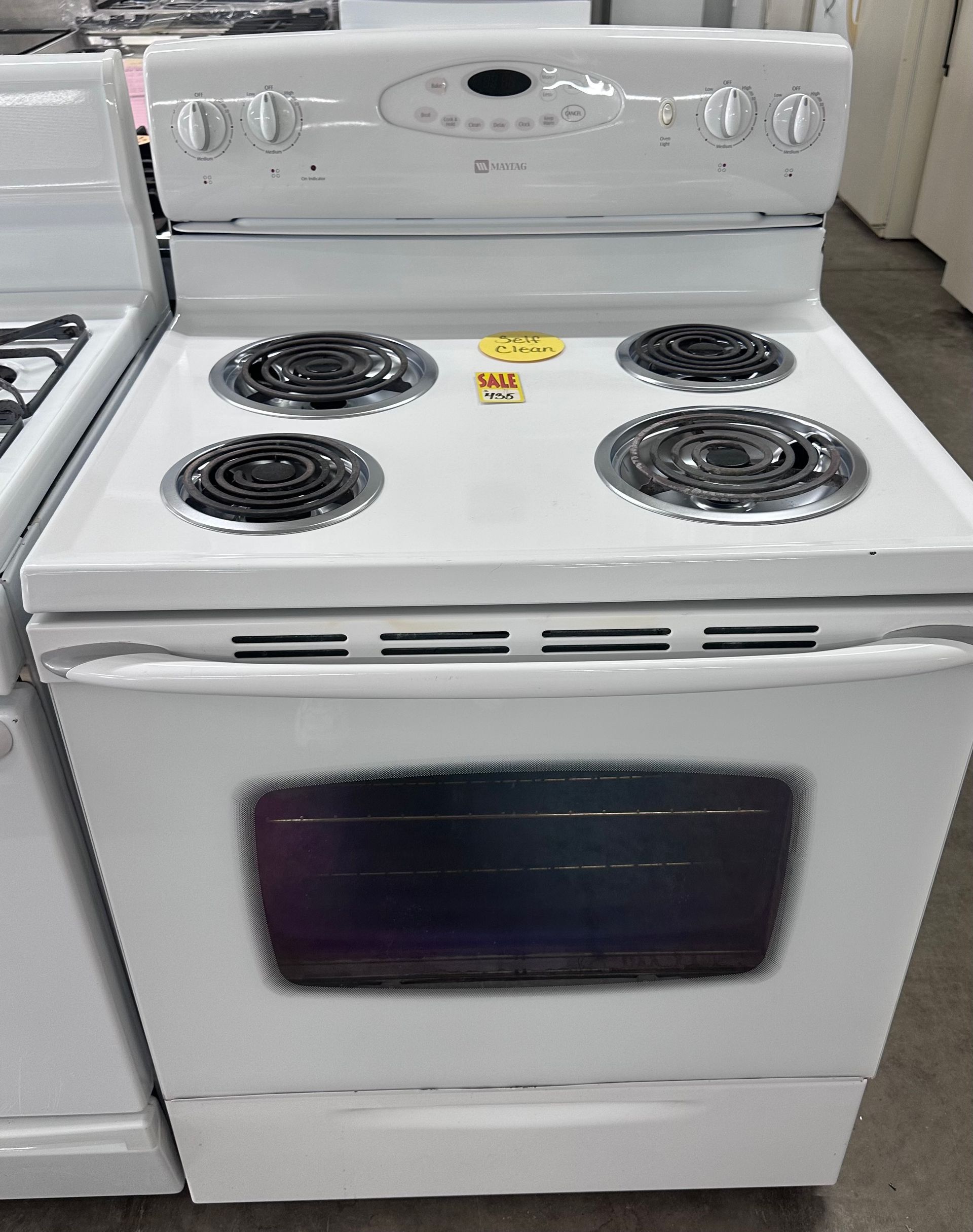 White electric stove with four coil burners and oven door, shown in a store aisle.