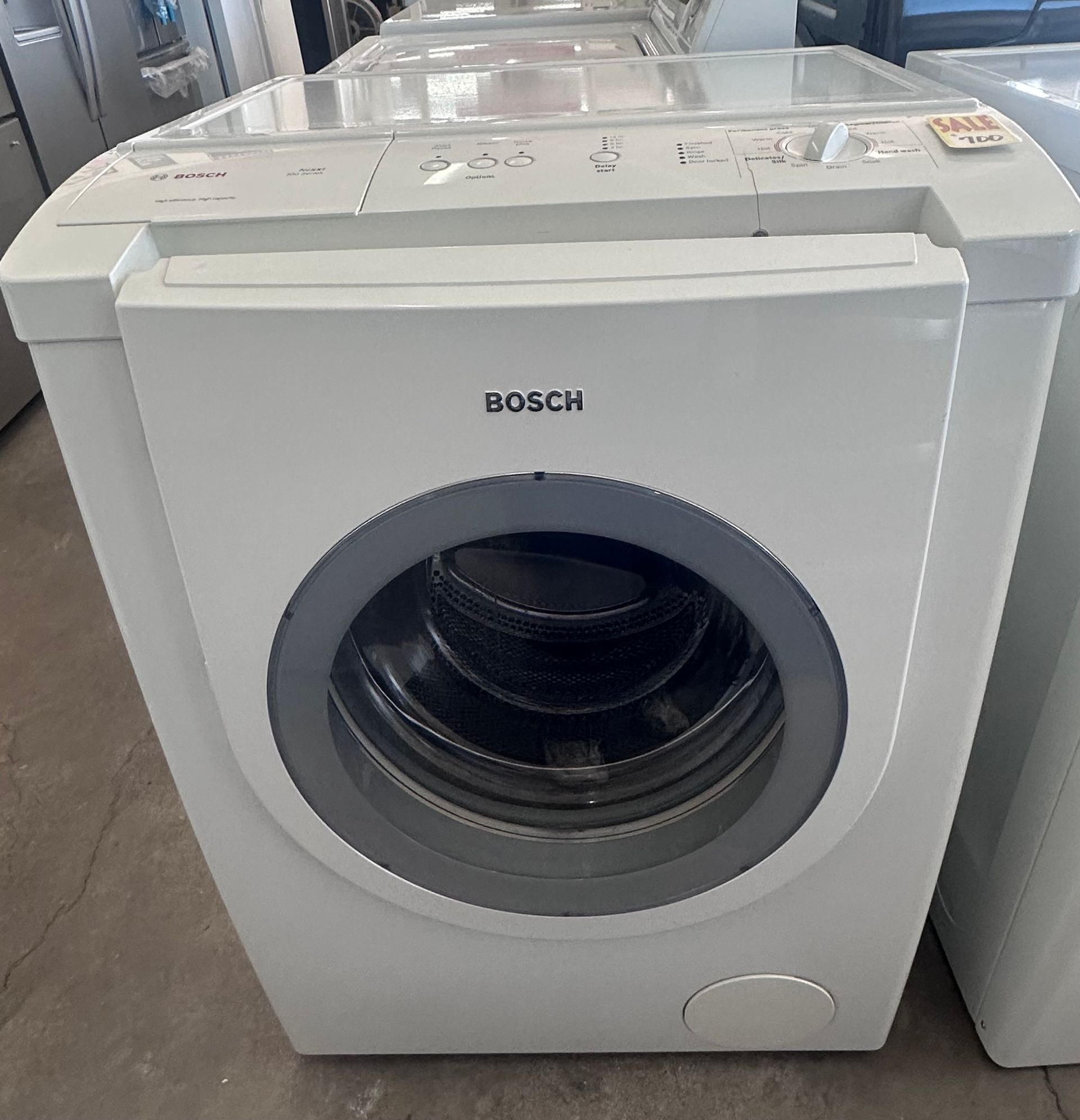 A white washing machine with the lid open is sitting next to another washing machine.