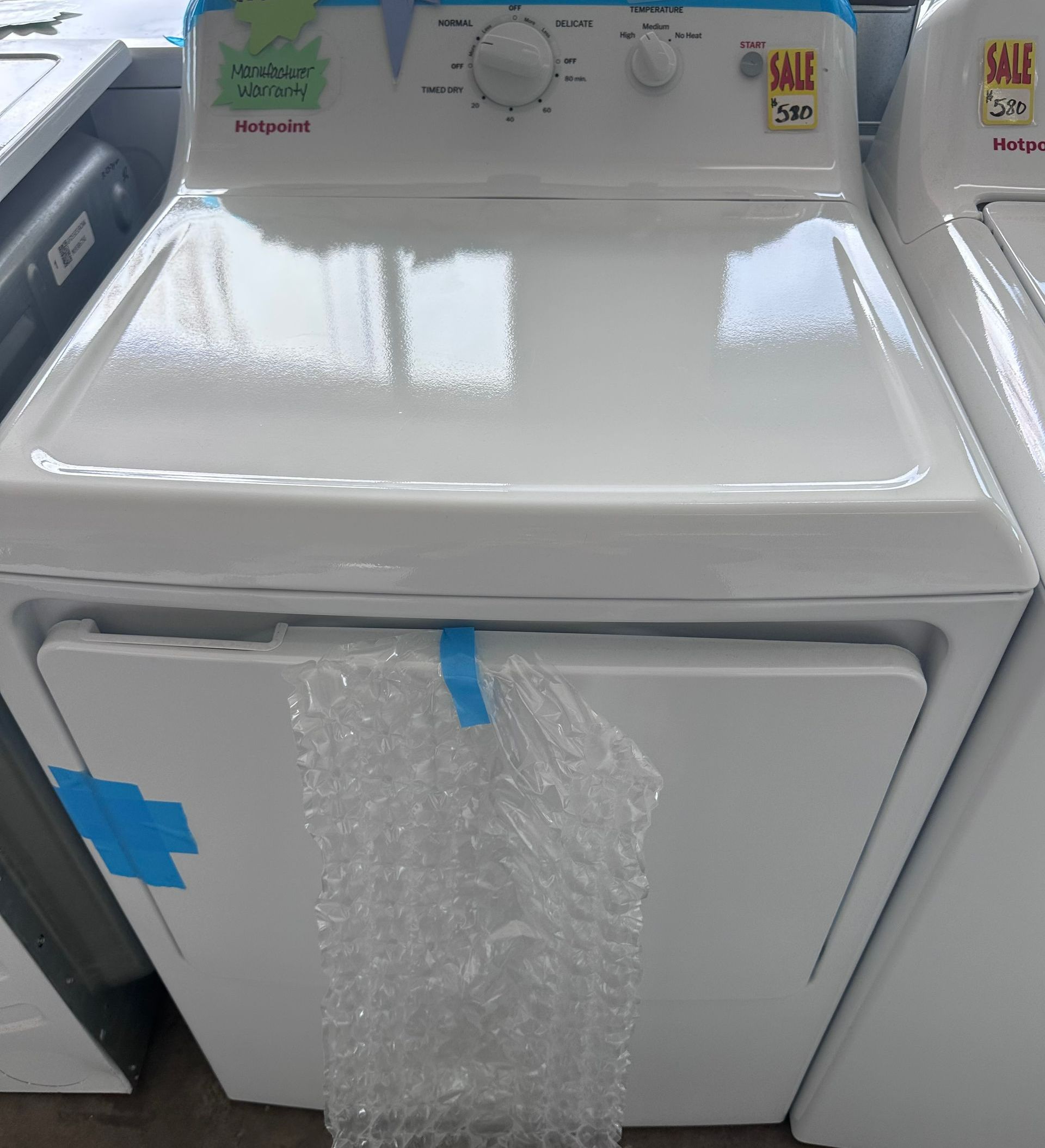 White electric clothes dryer with controls on top, a sale sticker, and bubble wrap.
