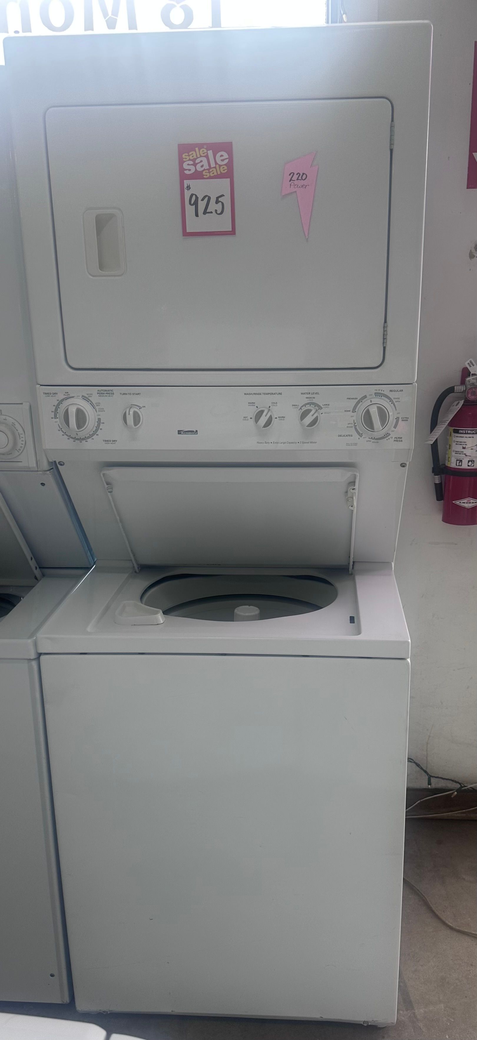 White stacked washer and dryer in a laundry room, with the dryer door open and a washer below.
