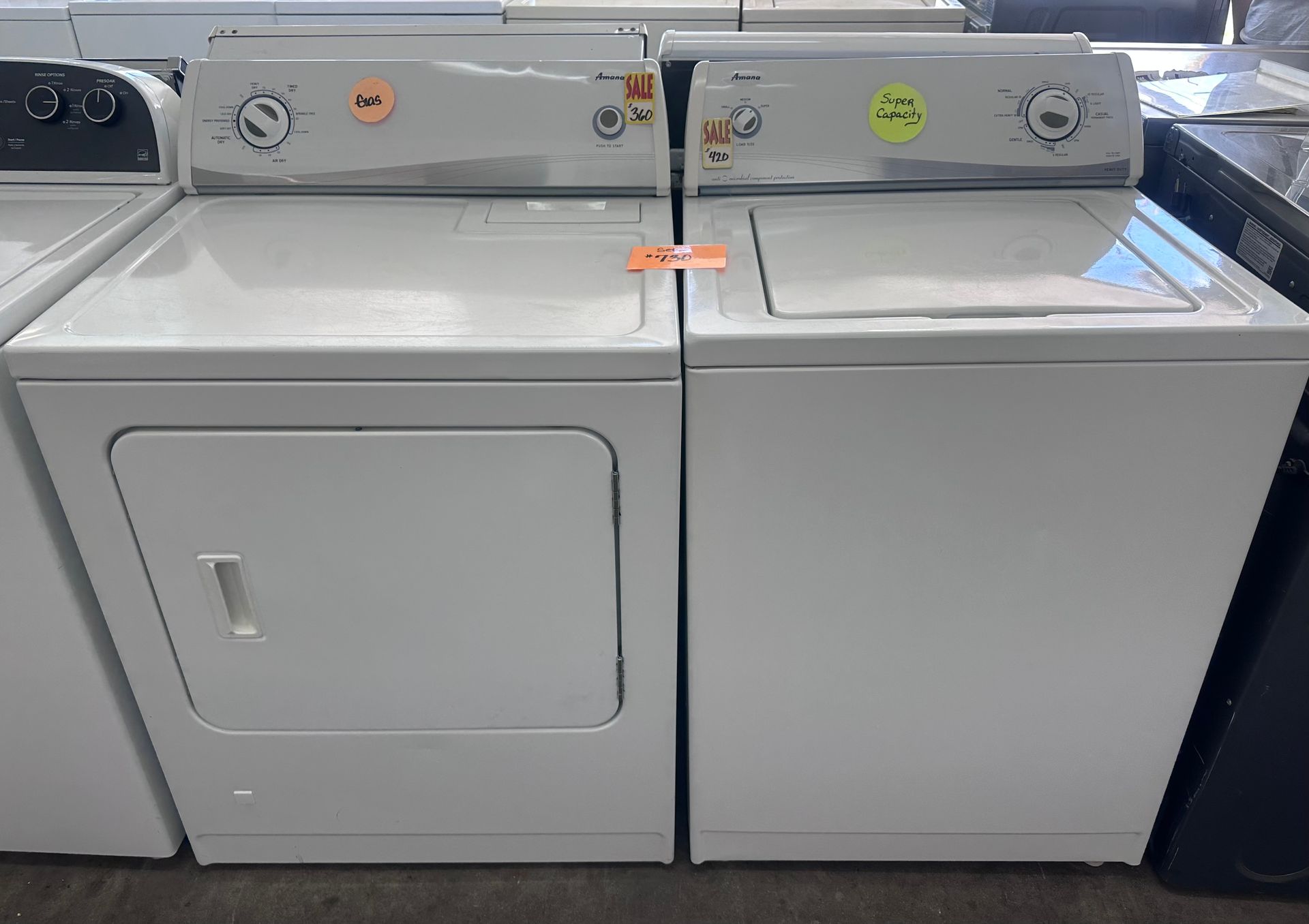 A white washing machine with the lid open is sitting next to another washing machine.