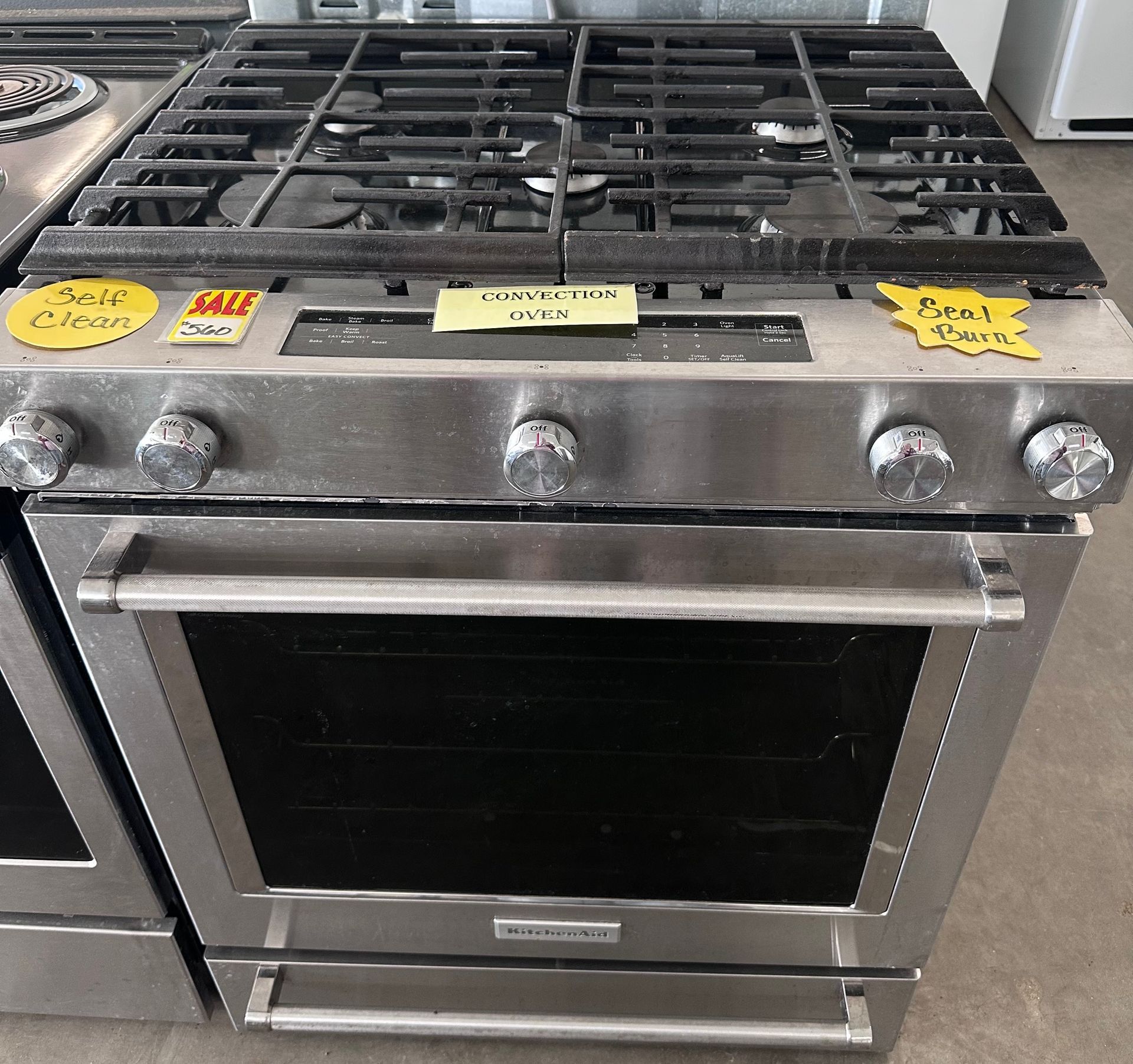 Stainless steel gas range with oven, burners, and control knobs, with sale stickers.