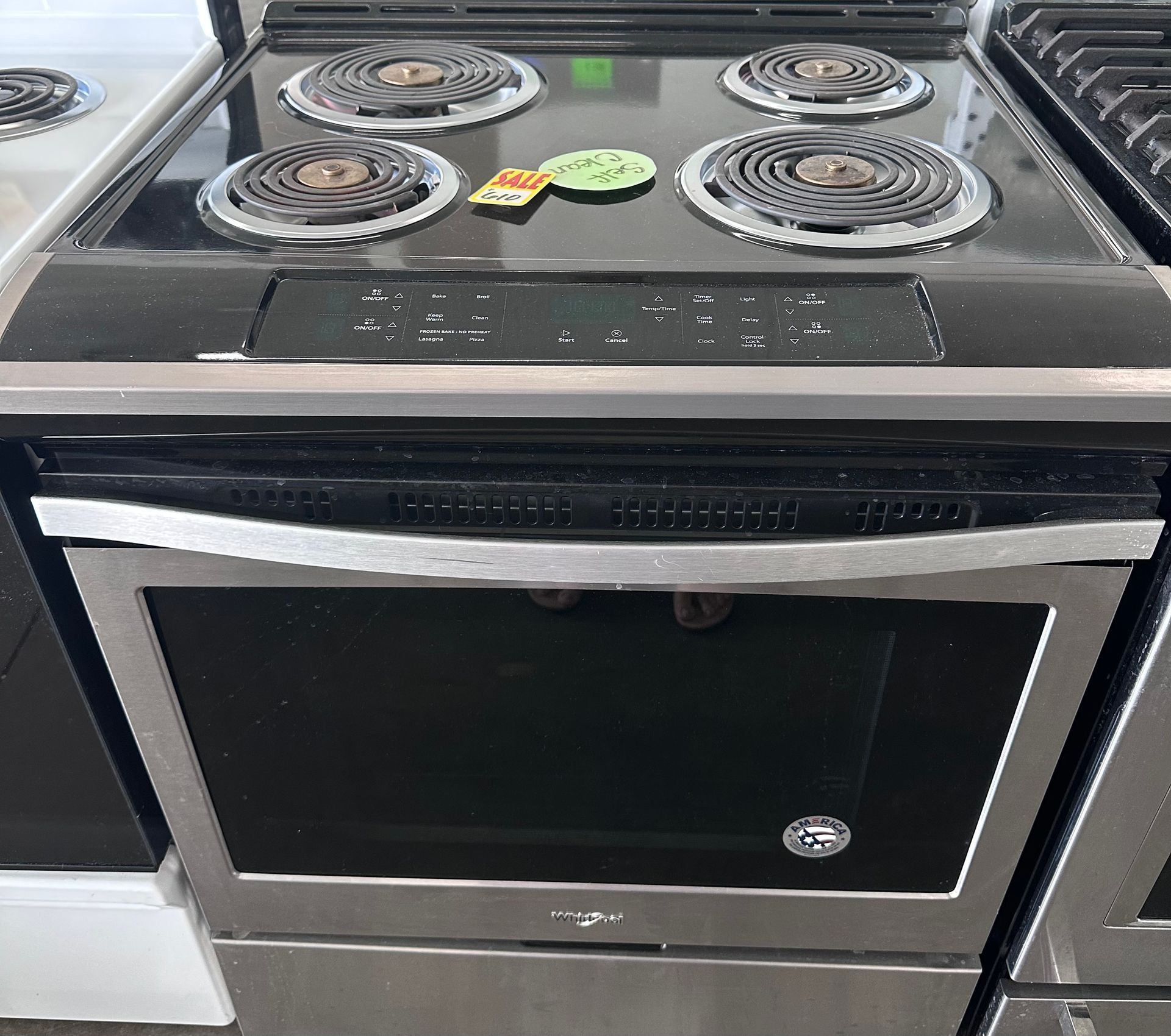 Stainless steel Whirlpool electric range with black cooktop, four burners, and oven.