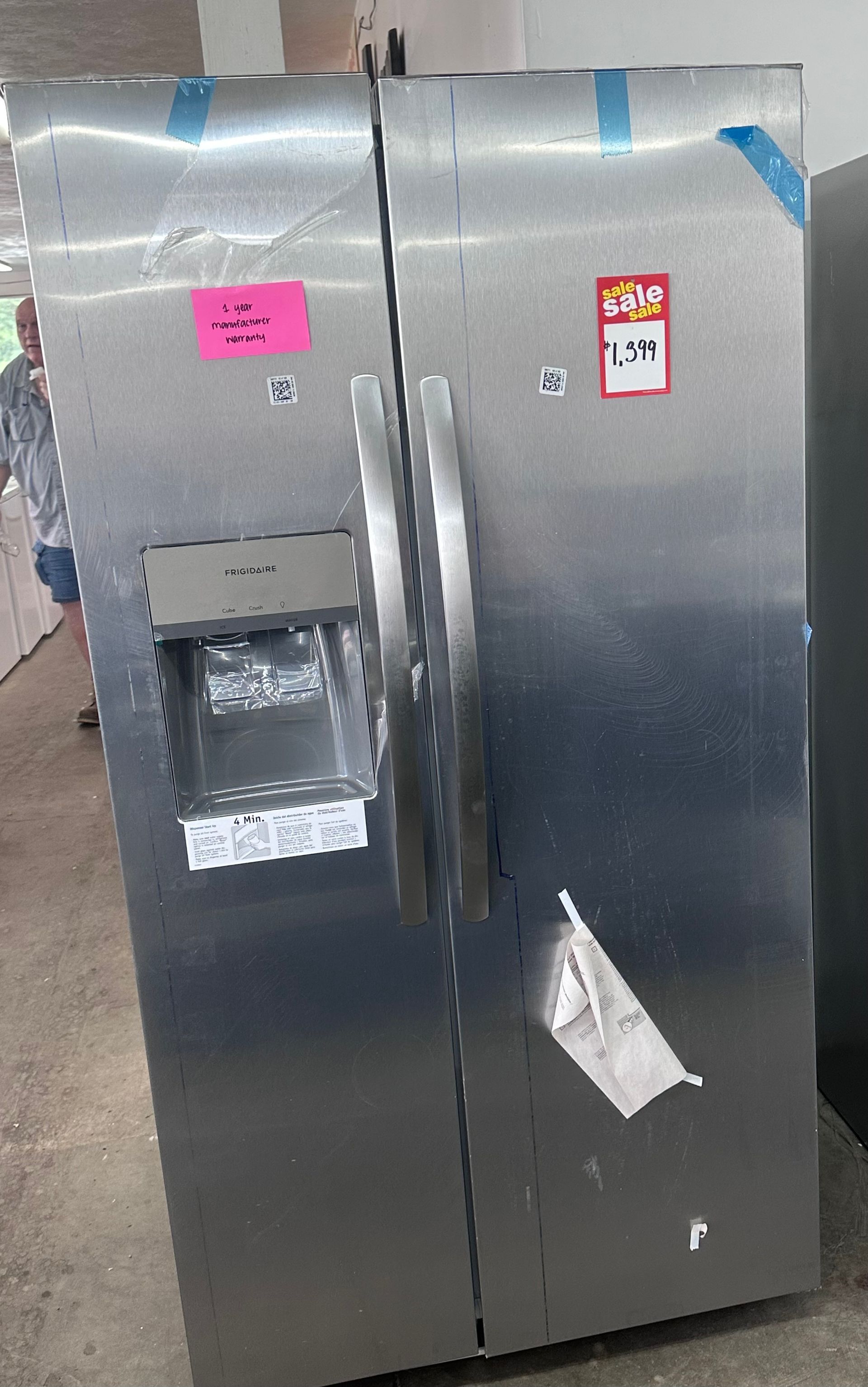 Stainless steel double-door refrigerator with a built-in water dispenser and small posted labels