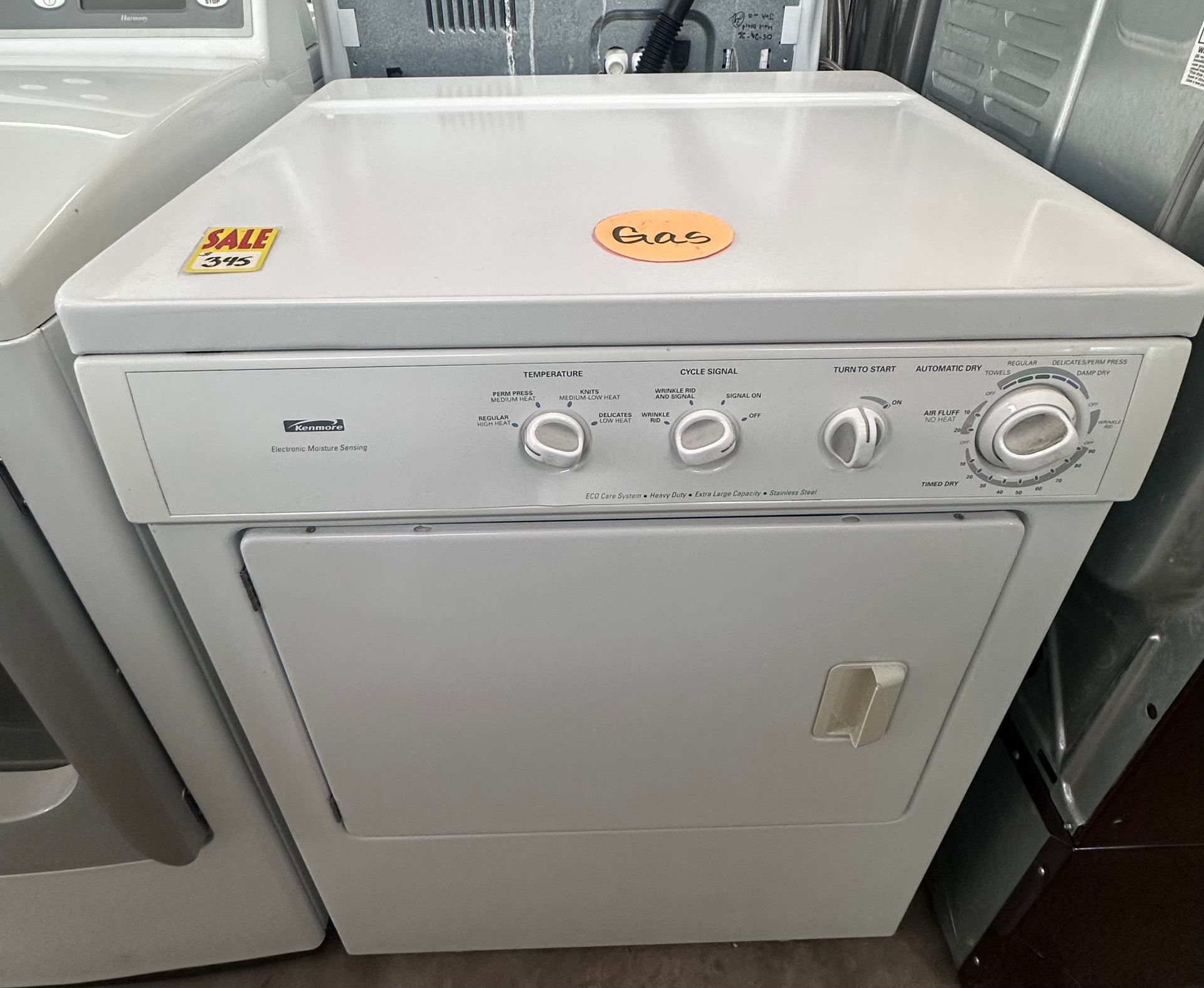 A white dryer is sitting on top of a counter next to a washer and dryer.