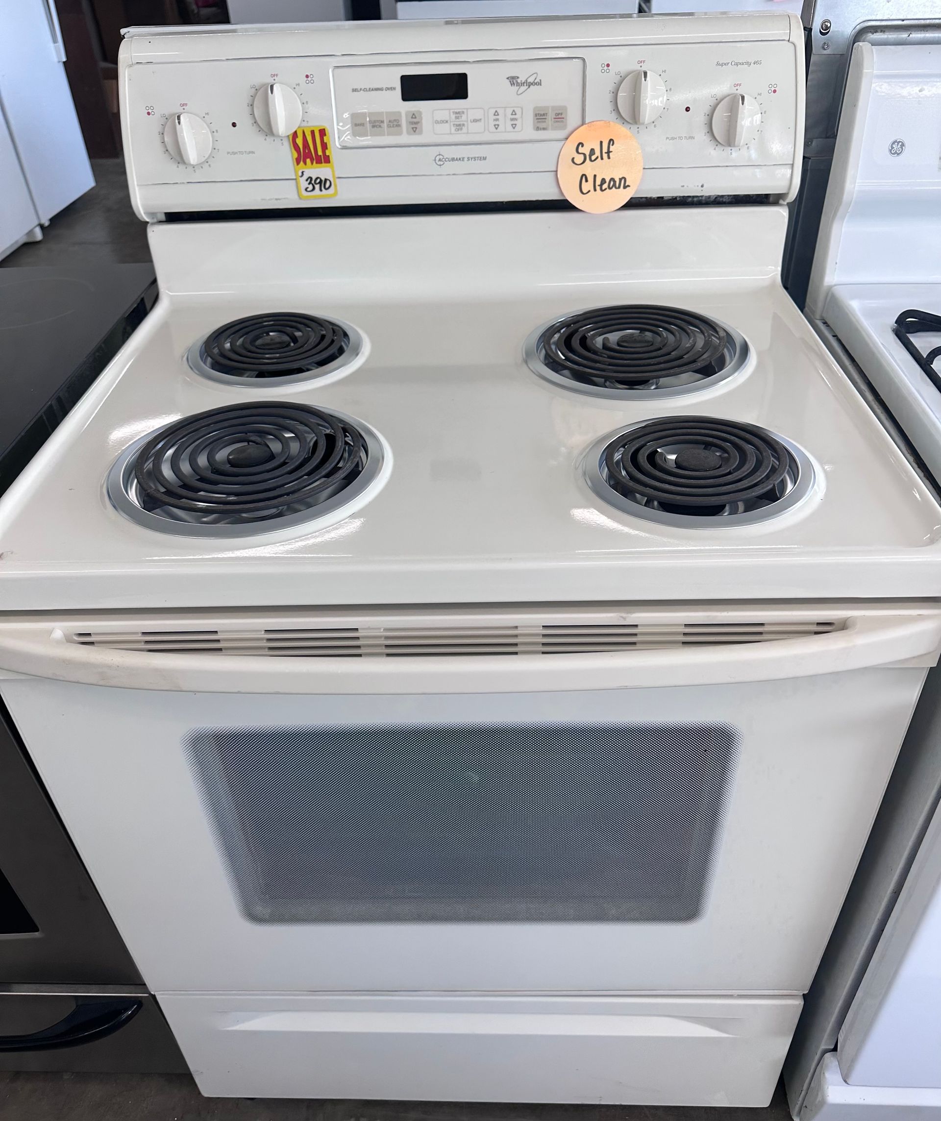 White Whirlpool electric range with four burners and a self-cleaning oven, in a store.