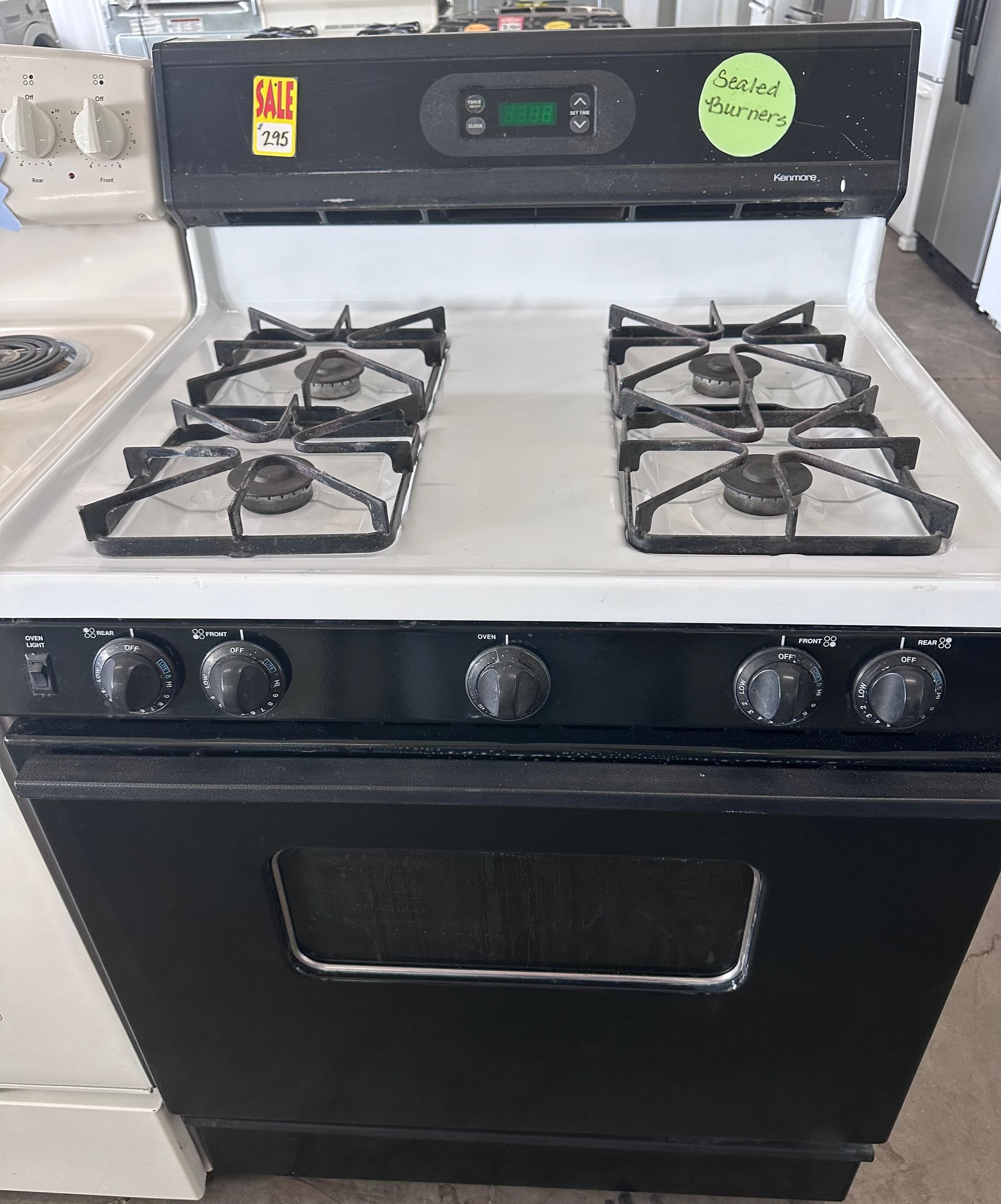 Black and white gas range with four burners, oven, and control panel.