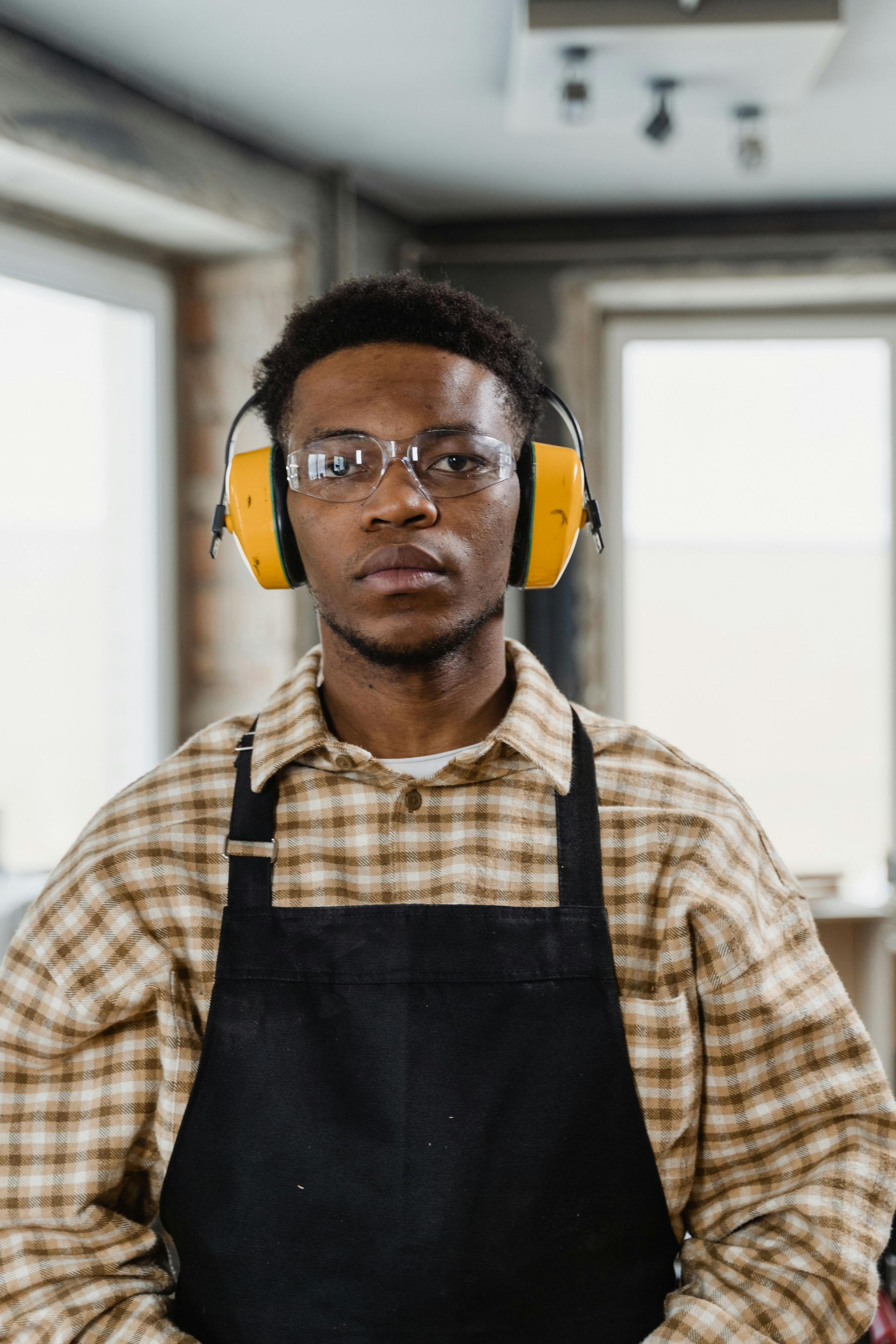 Man in workshop, wearing safety glasses, earmuffs, and apron.