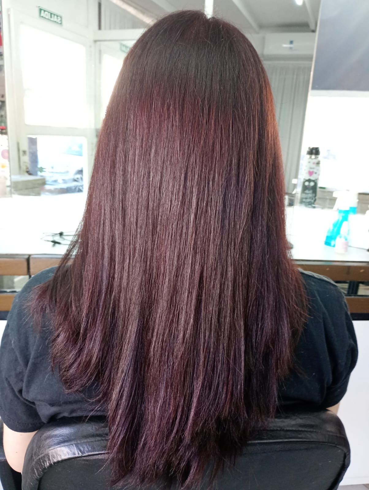 Mujer con cabello largo y oscuro de color burdeos sentada en una silla de salón.