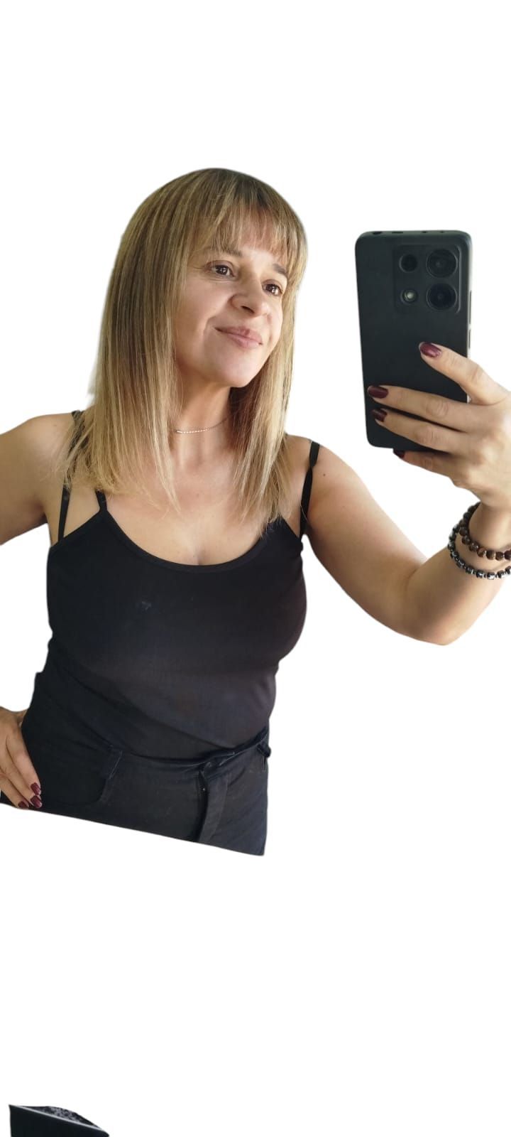 Mujer tomándose una selfie, vestida con un top y pantalones negros, sosteniendo un teléfono negro, cabello rubio.
