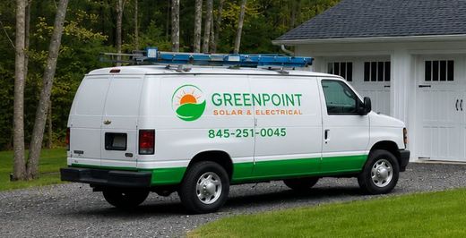 Greenpoint service van parked on a driveway beside a house, with ladder rack on top.