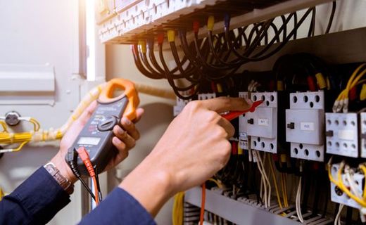 Technician testing electrical control panel with a multimeter inside a wiring cabinet