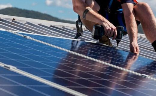 Worker installing solar panels on a rooftop with a power drill