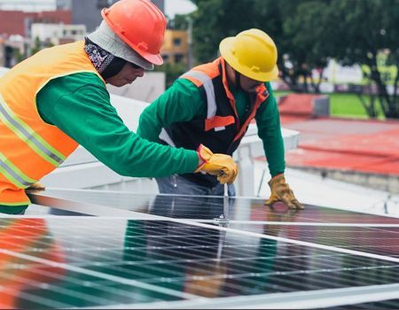 Two workers in hard hats installing solar panels on a rooftop