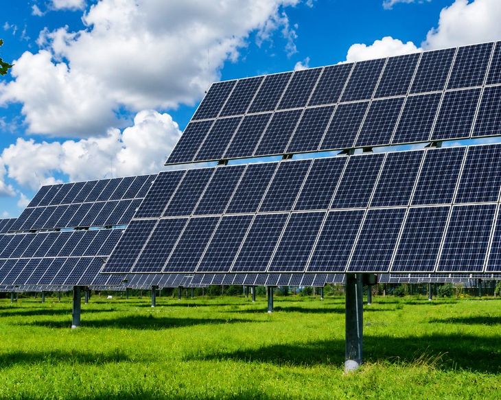 Solar panels on a grassy field under a blue sky with clouds.