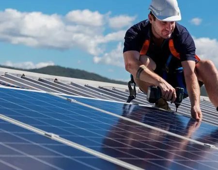 Worker installing solar panels on a rooftop under a blue sky