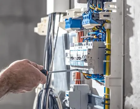 Hand using a screwdriver on an electrical breaker panel with blue wiring