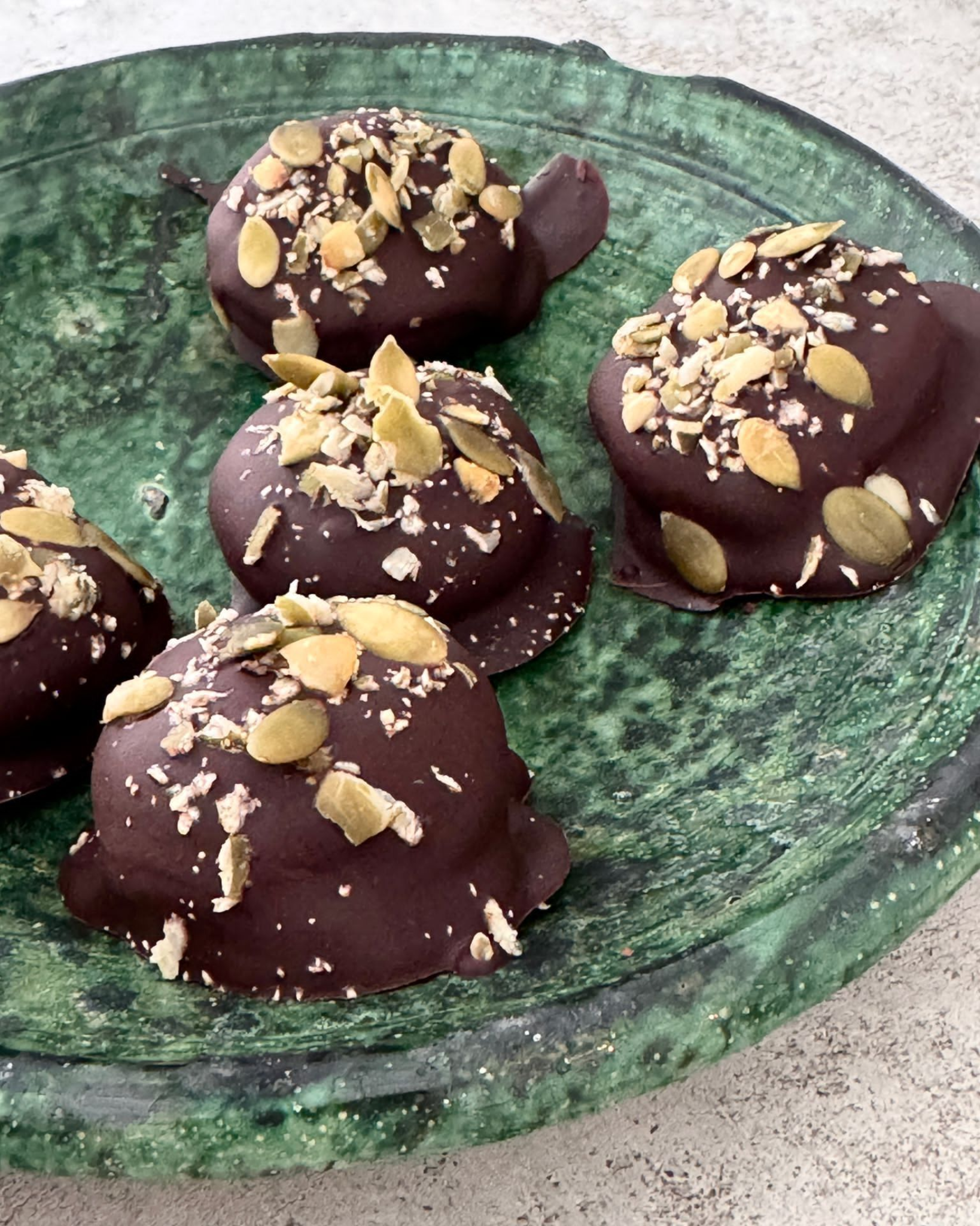 Chocoladeschildpadjes op een groen, gestructureerd bord, bestrooid met zaadjes.